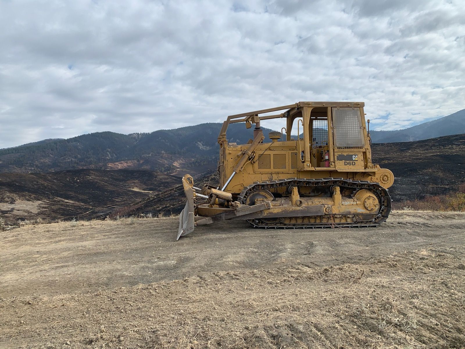 A bulldozer is parked in a dirt field with mountains in the background.
