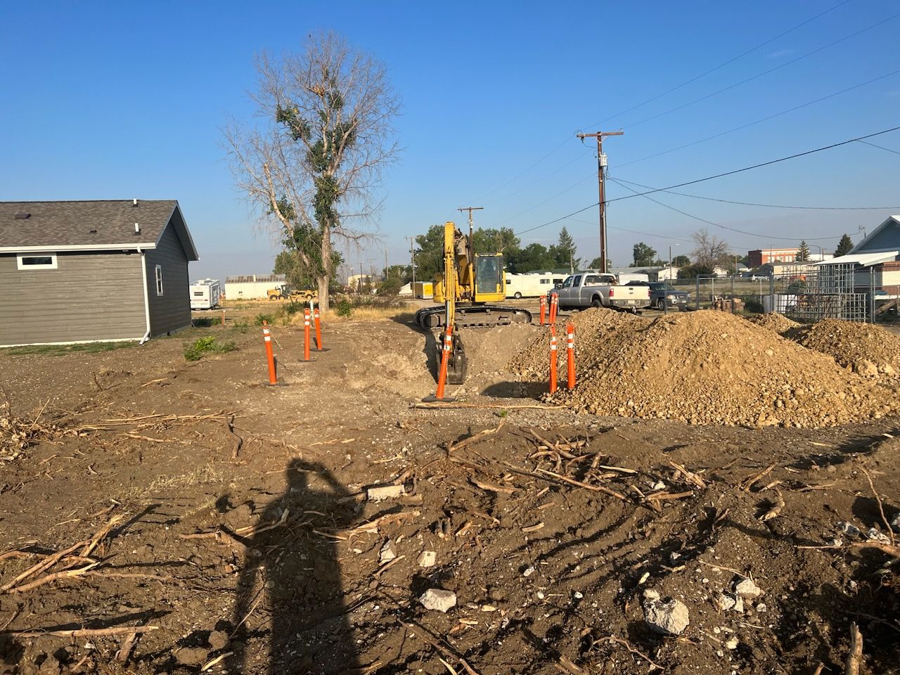 Construction site with a yellow excavator, wood chips, and a small building.