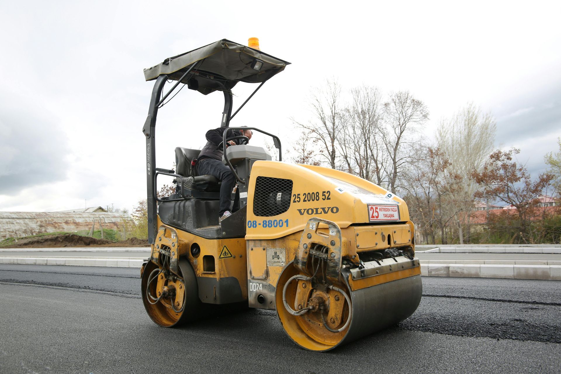 Yellow Volvo road roller compacting asphalt on a paved road.