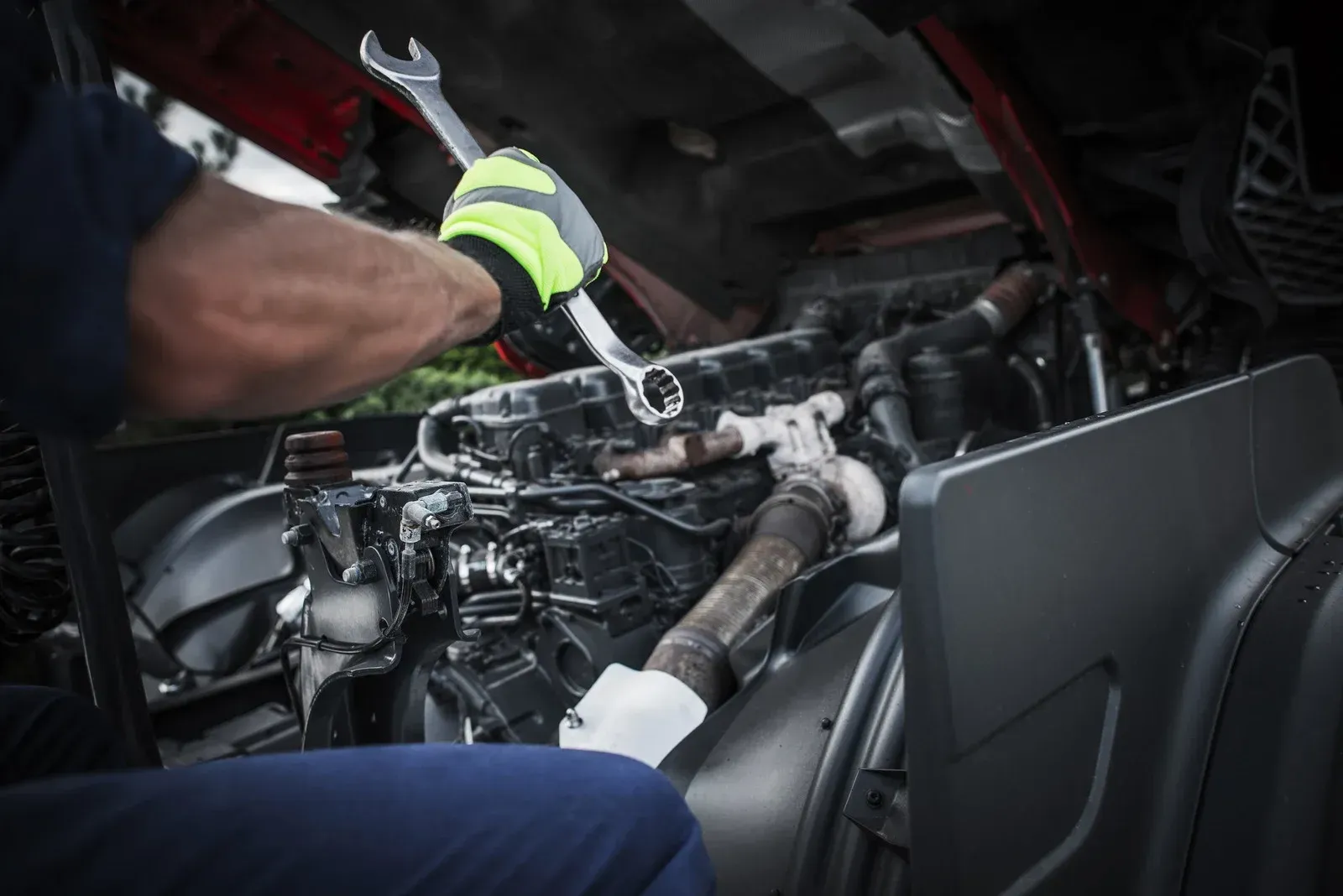Mechanic working on a truck engine with a wrench, wearing gloves.