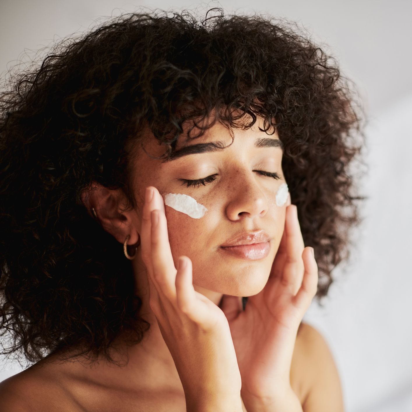A woman with curly hair is applying cream to her face.