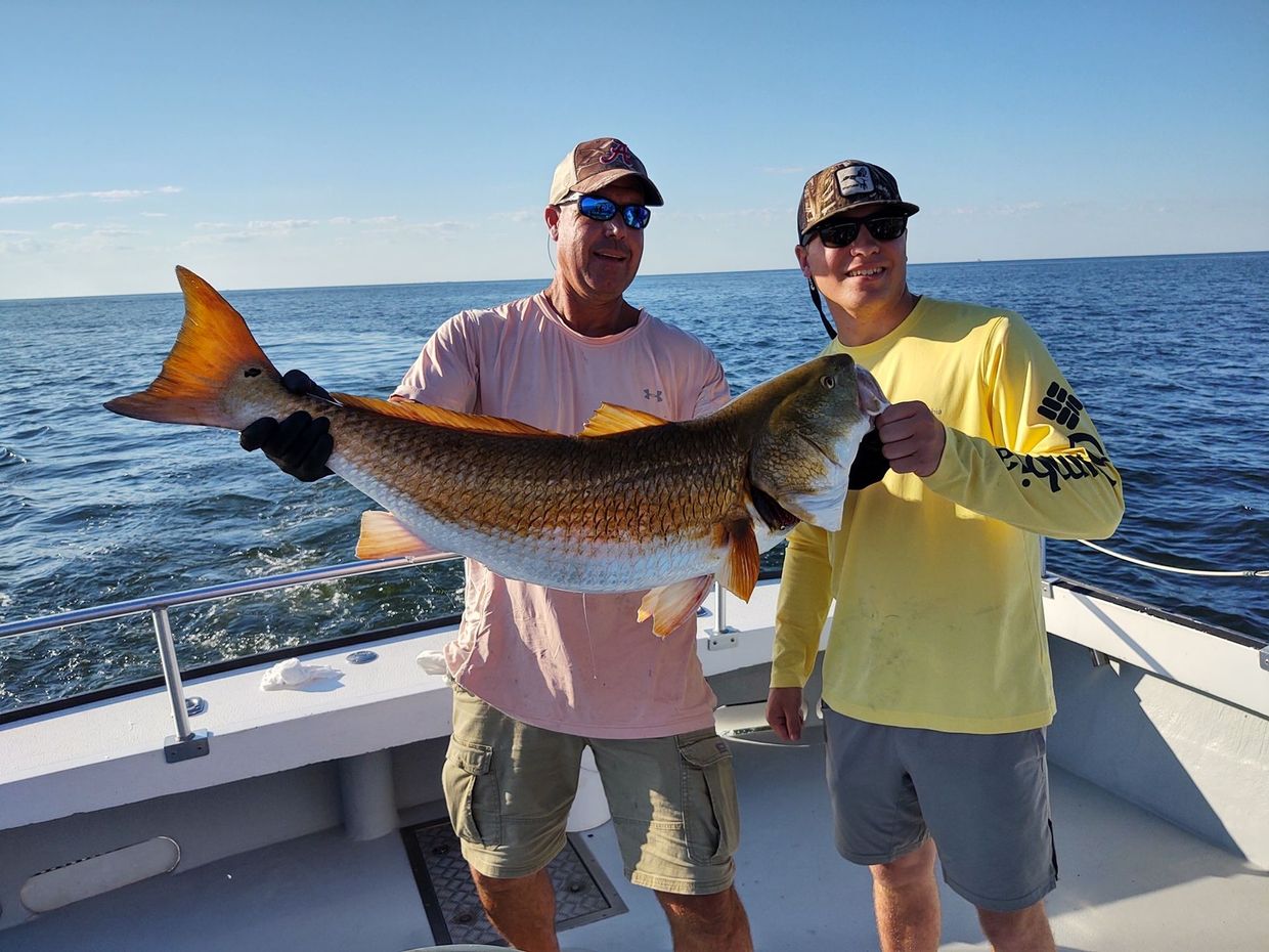 Two men are standing on a boat holding a large fish.