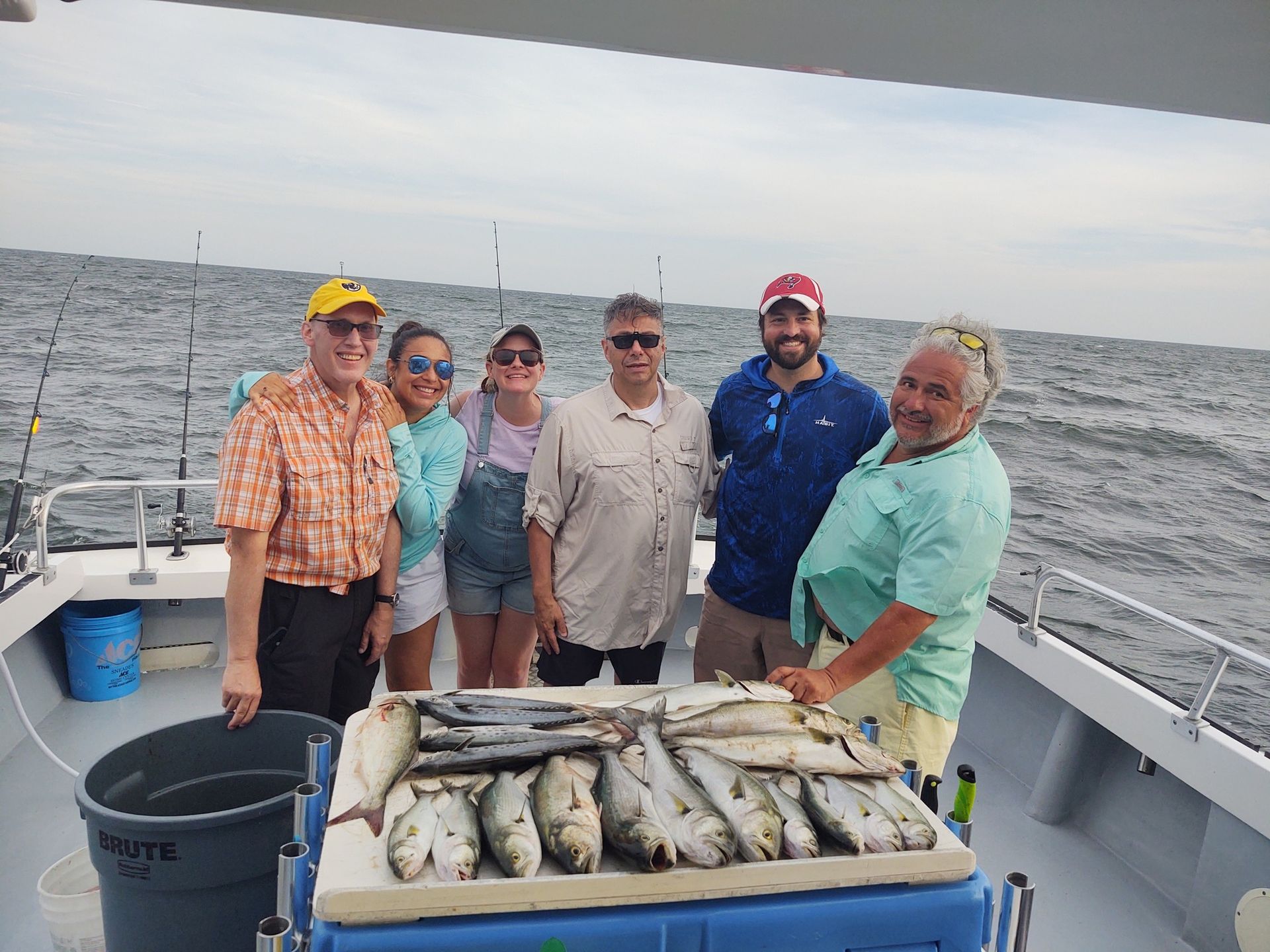 A group of people are standing on a boat with a cooler full of fish.