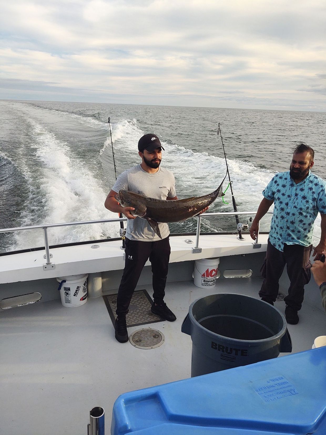 Two men are standing on a boat holding a large fish.