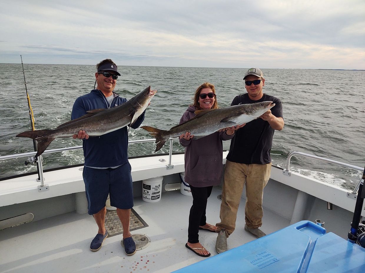 Three people are standing on a boat holding large fish.