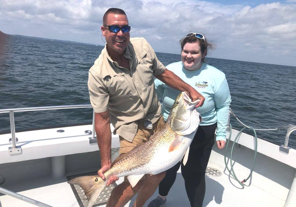 A man and a woman are holding a large fish on a boat.