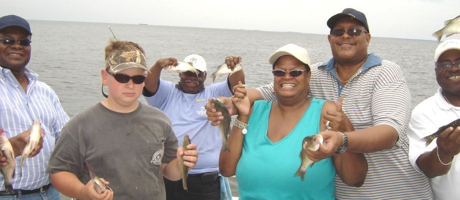 A group of people holding fish with the bay in the background.