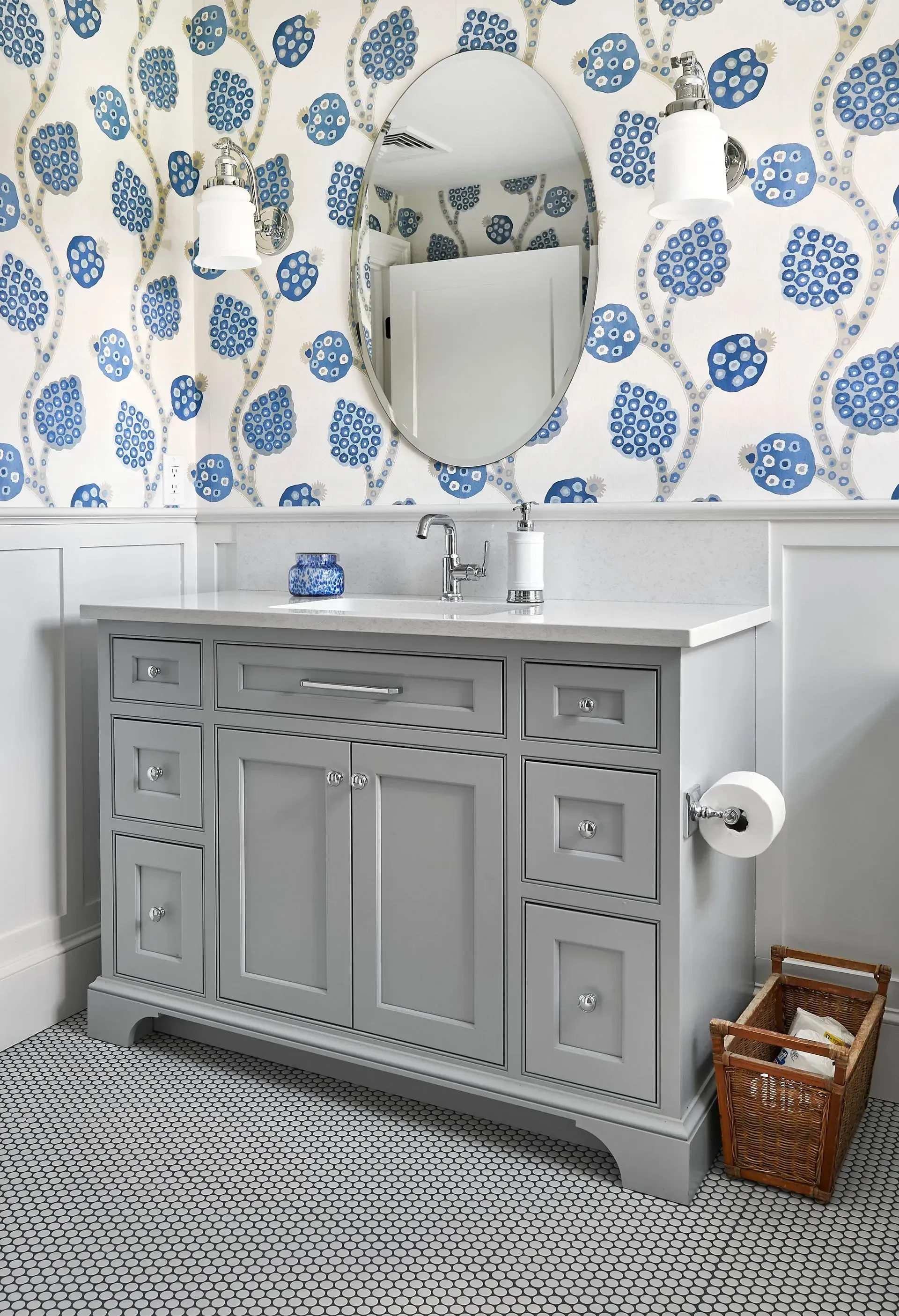 Gray vanity with white countertop in bathroom with blue floral wallpaper and a basket of towels.
