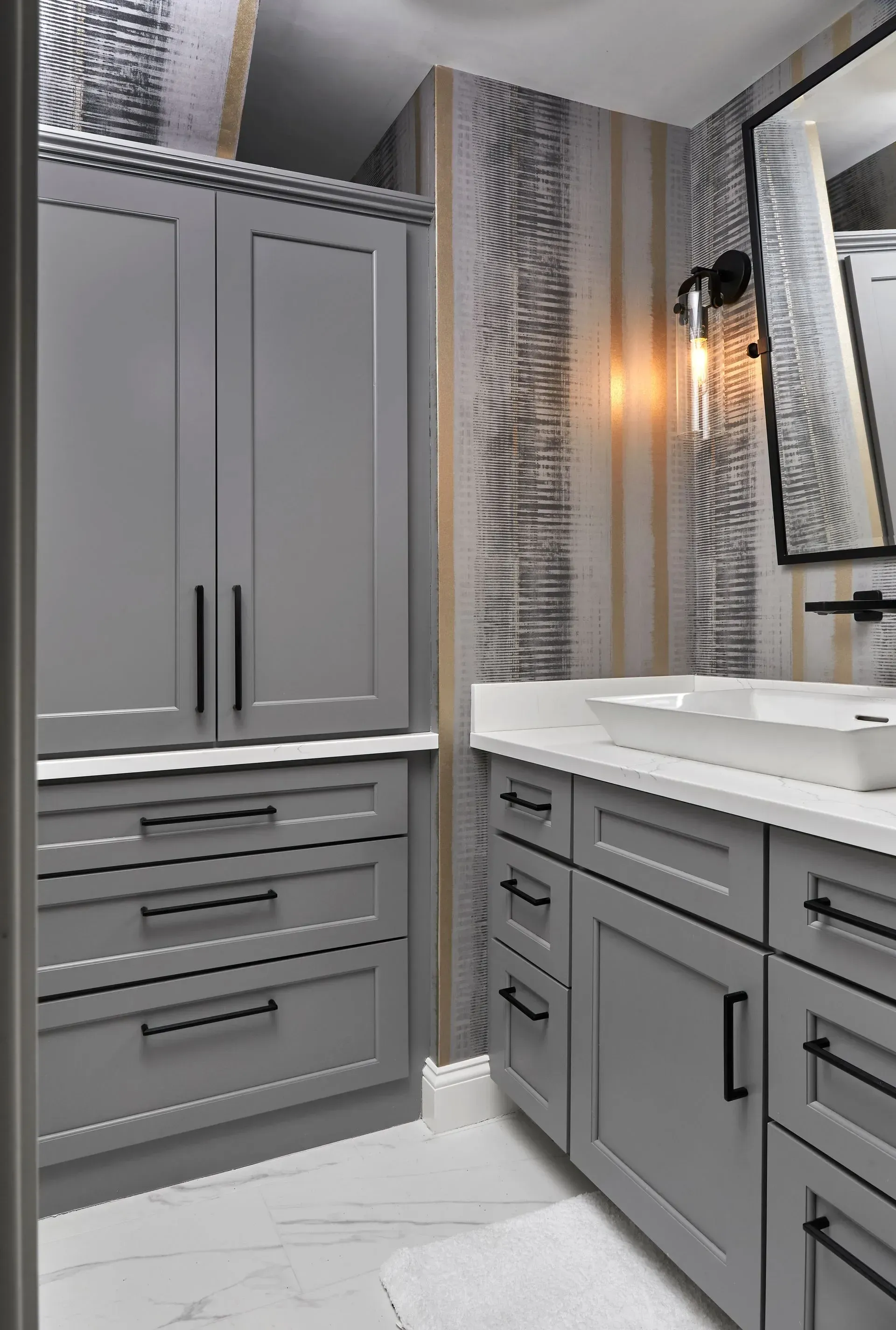 Gray bathroom with cabinets, white countertop, and patterned wallpaper.
