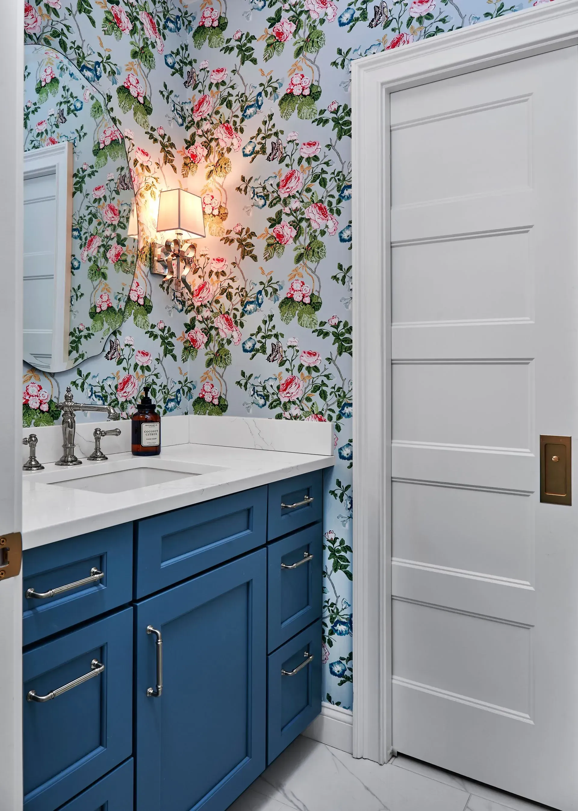 Blue vanity with white countertop and floral wallpaper in a bathroom. White door on the right.