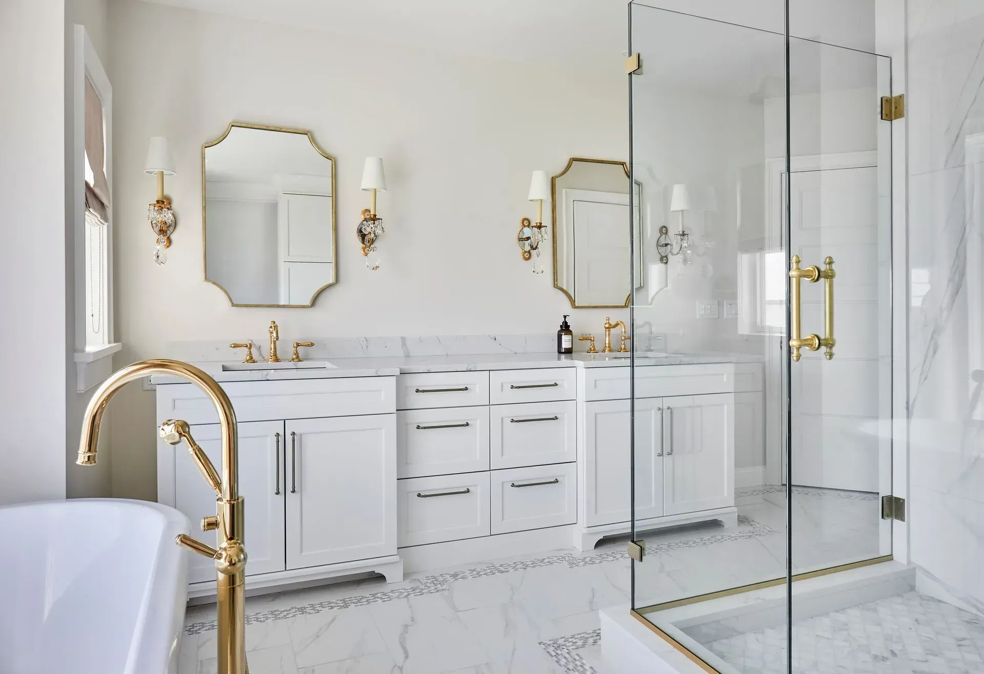 Elegant white and gold bathroom with double vanity, mirrors, and glass shower.