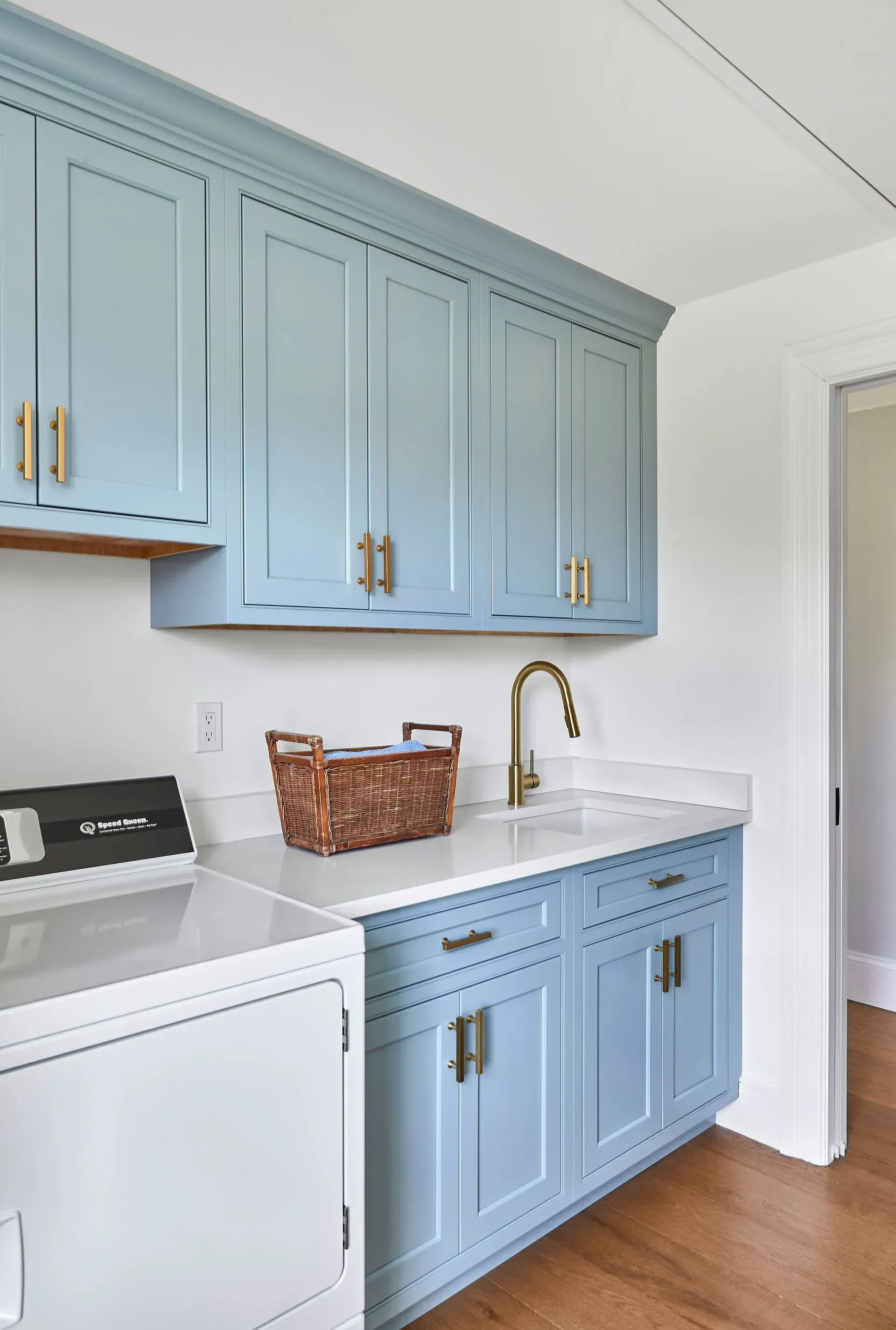 Blue laundry room cabinets with gold hardware and white countertop; a sink and a washing machine are visible.