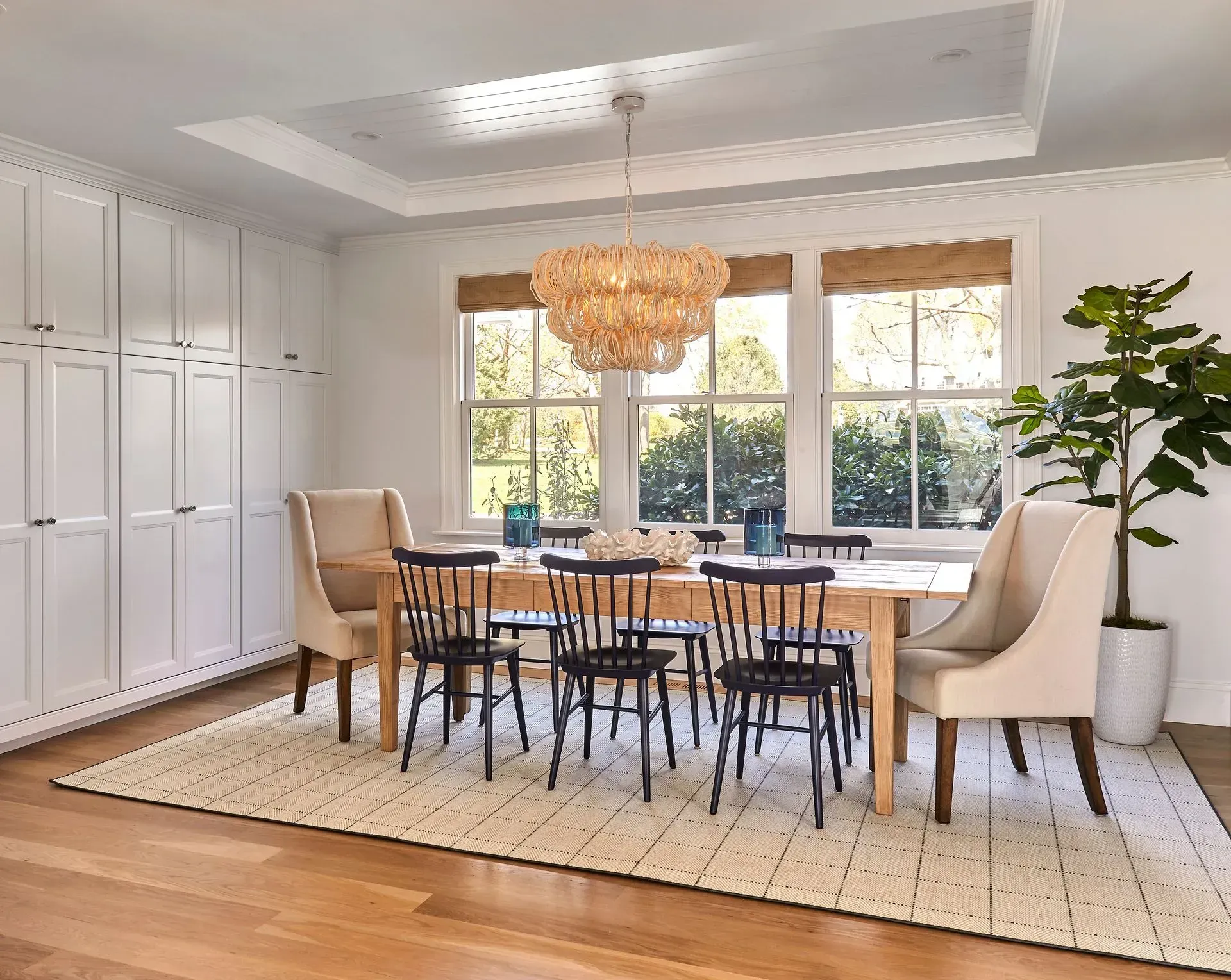 Dining room with a wooden table, chairs, and chandelier. White cabinets and a large window.