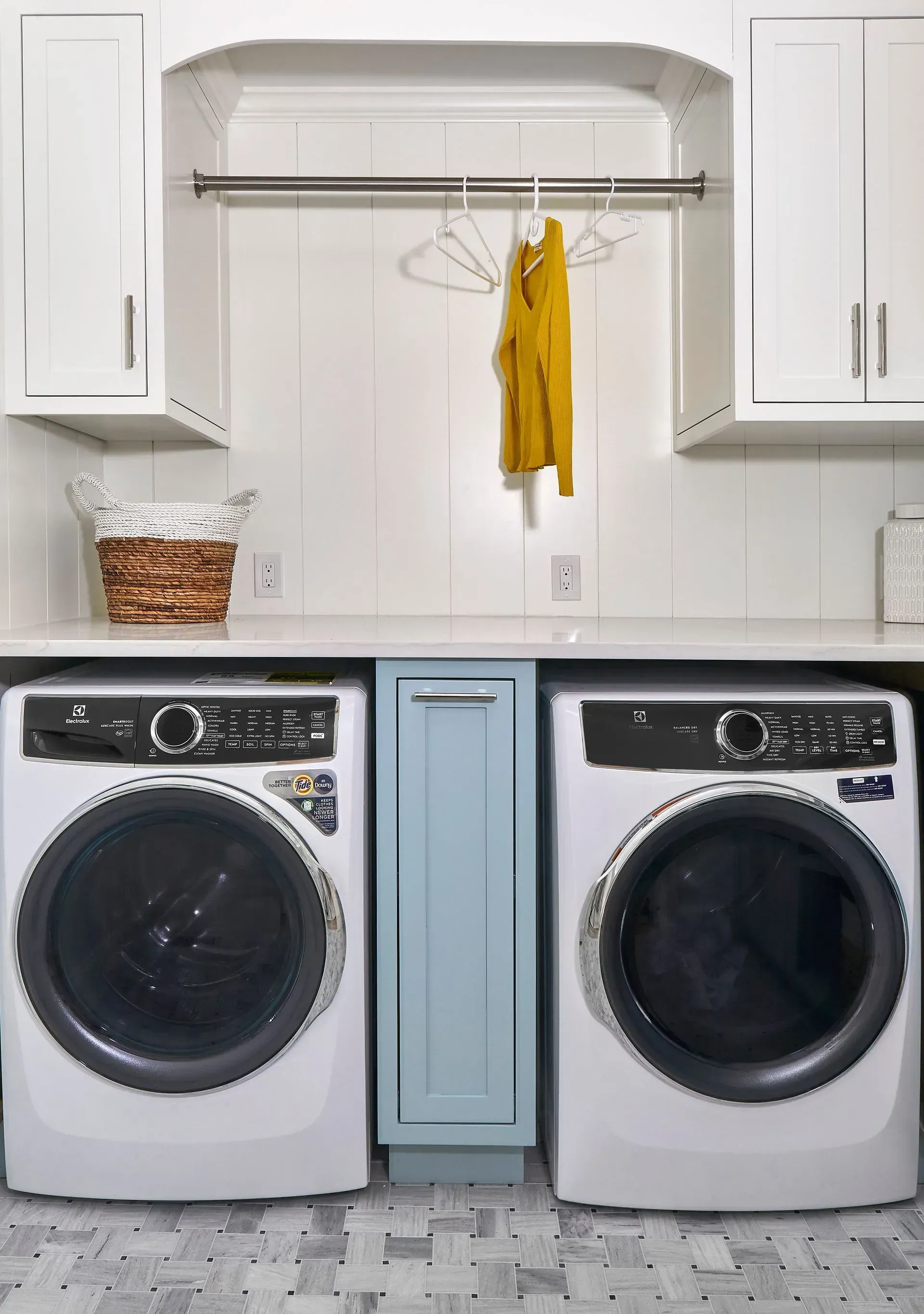Laundry room with a washer, dryer, and cabinets; yellow shirt hangs on a rod.