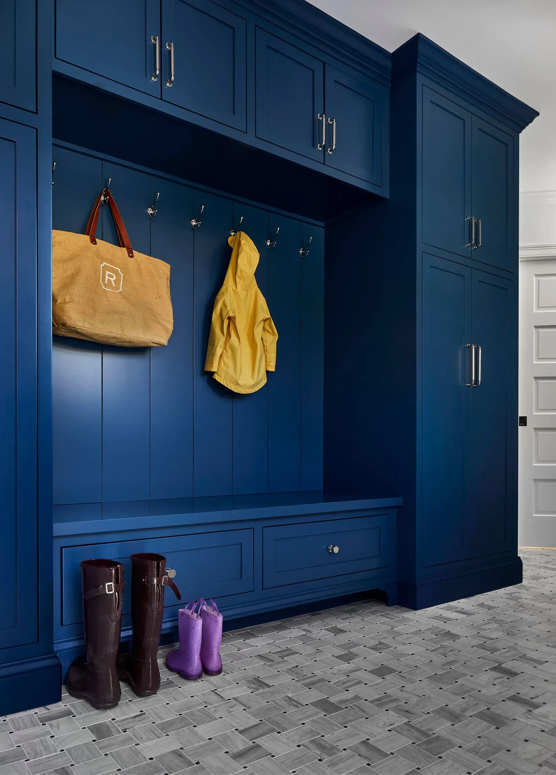 Blue storage unit with bench, hooks, and cabinets; boots and bags hang on it.