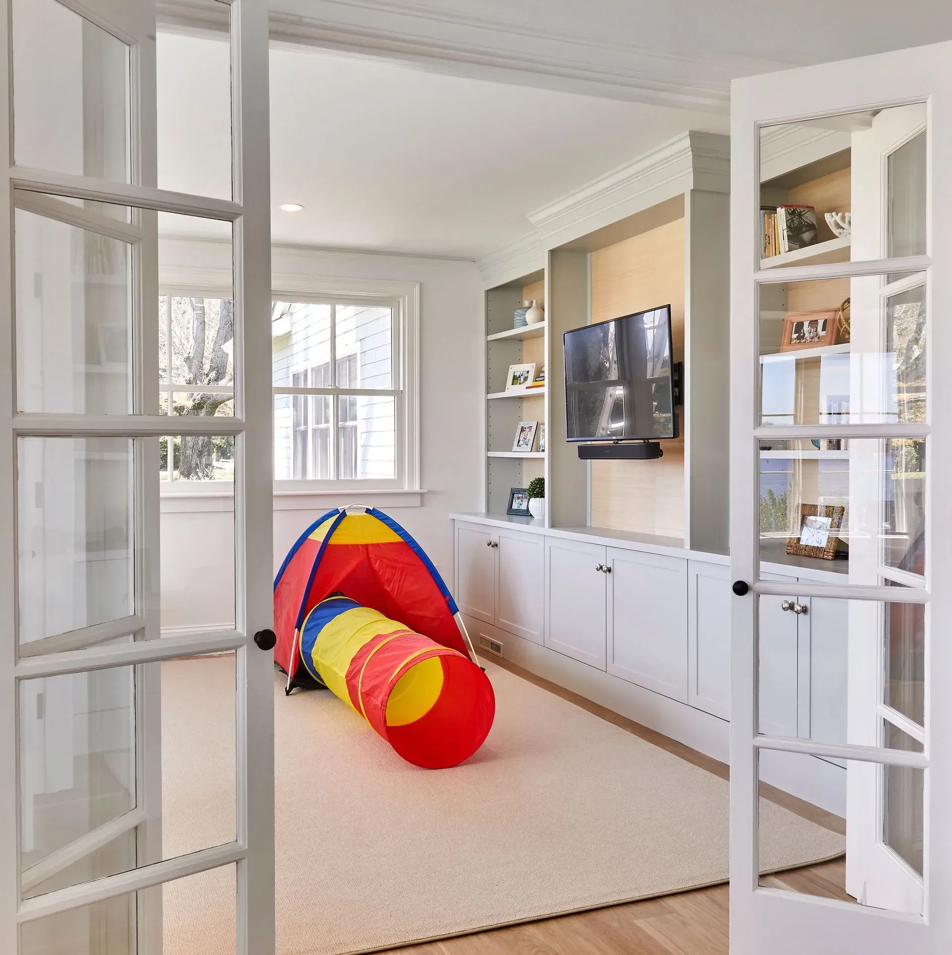 A playroom with an open tunnel, built-in cabinets, and a television. White doors are open to the room.