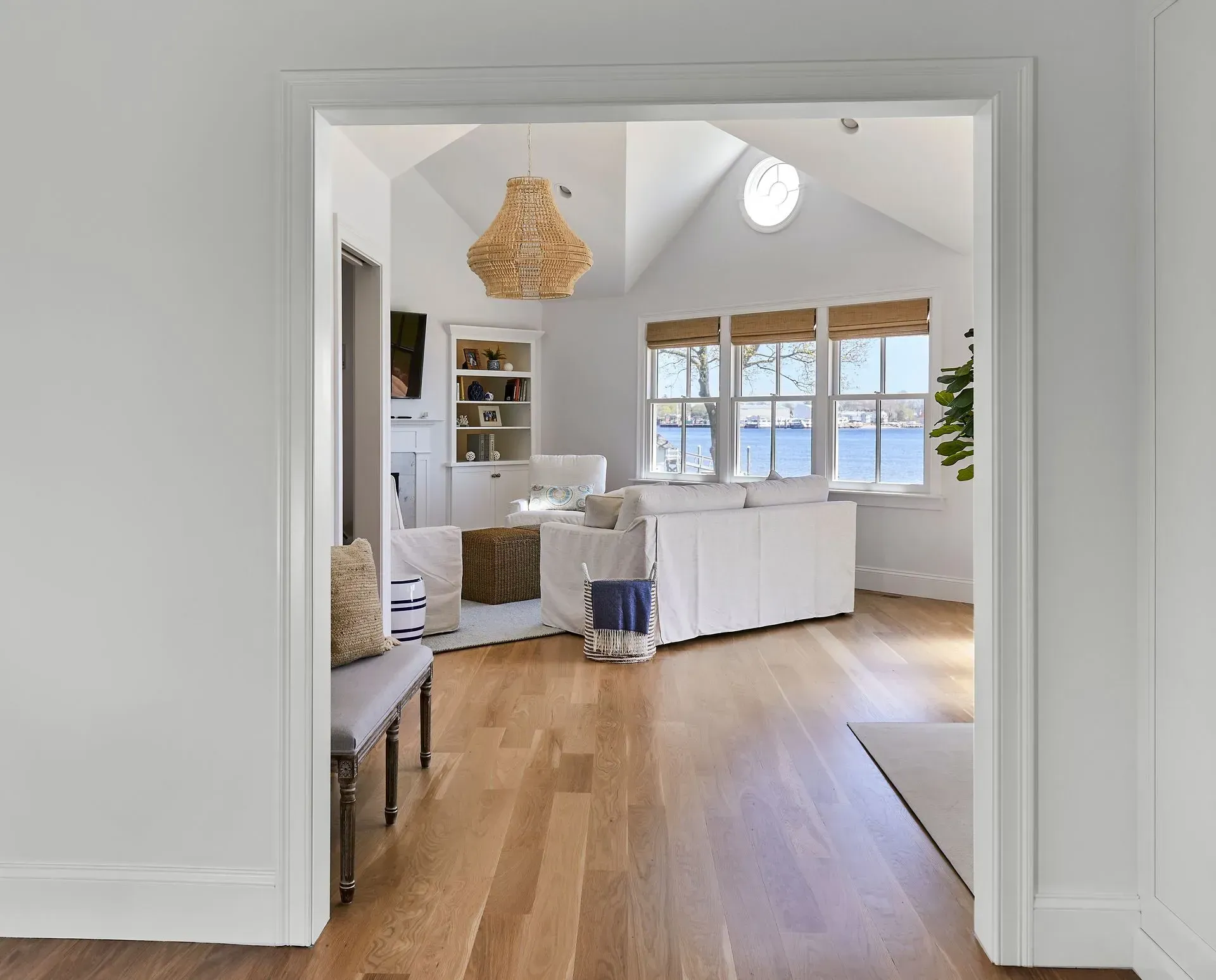 A doorway leads into a bright living room with a white couch and a view of water through windows.