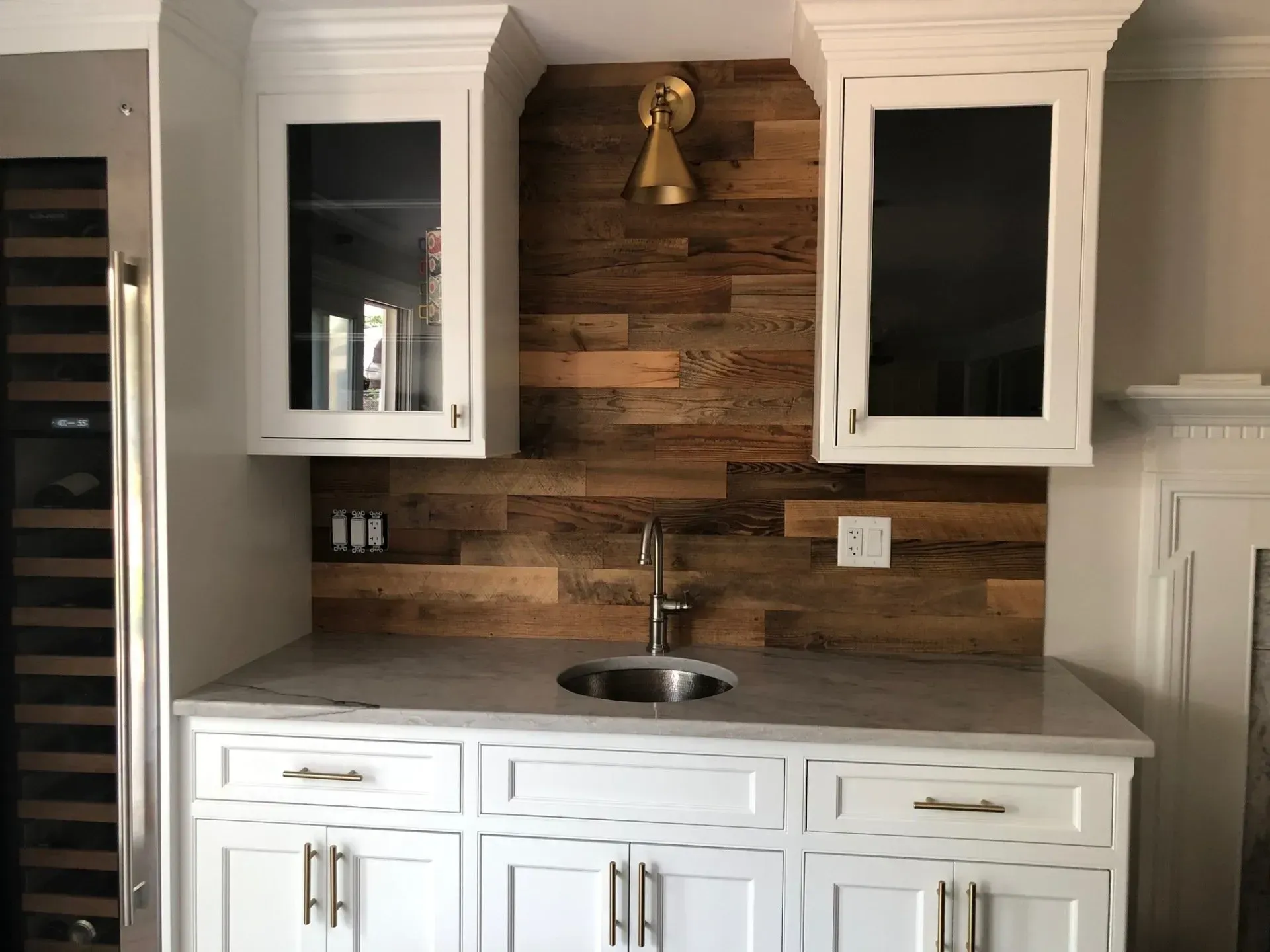 A built-in bar area with wood accent wall, white cabinets, and a sink.