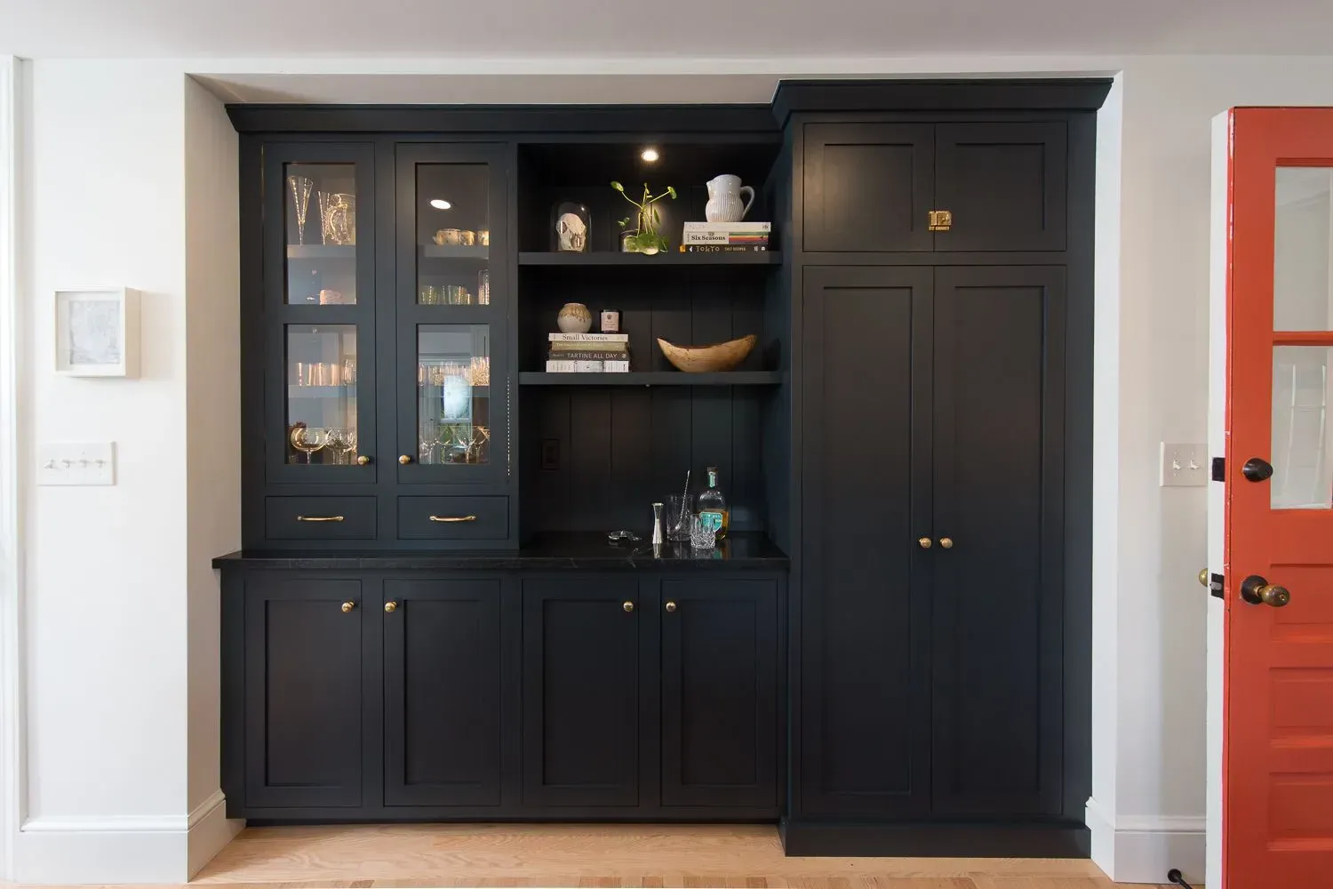 Black built-in cabinet with glass-fronted shelves, open shelves, and solid doors, next to a red door in a doorway.
