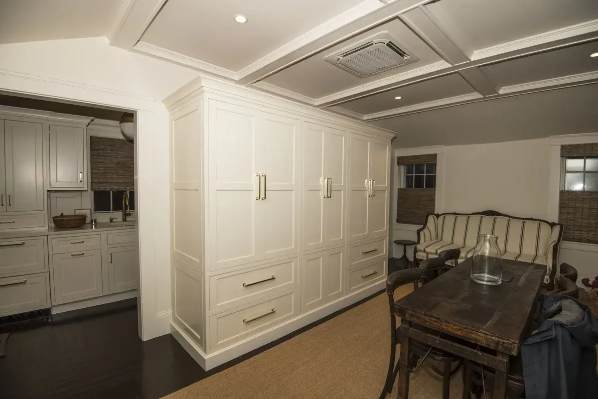 White cabinets in a room with a kitchen in the distance, a dining table, and a sofa.