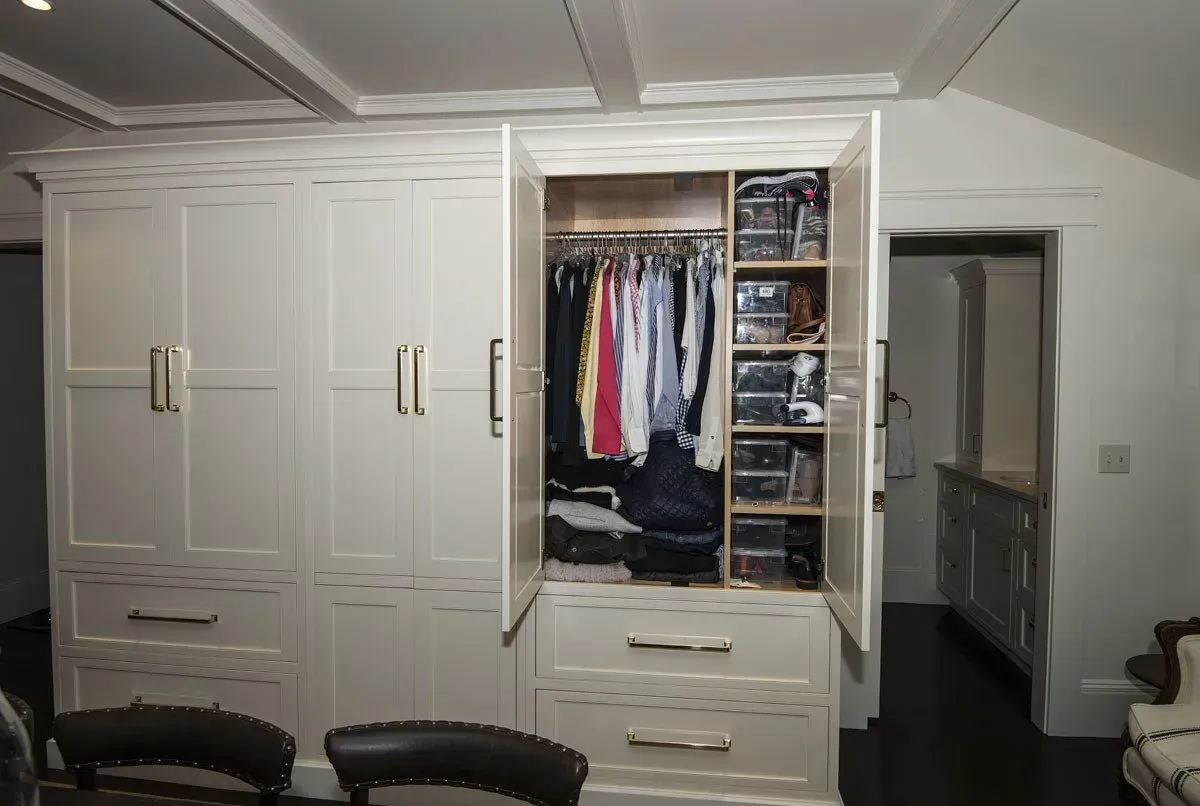 Cream-colored built-in closet with open doors, revealing hanging clothes and shelves. Dark wood floor.
