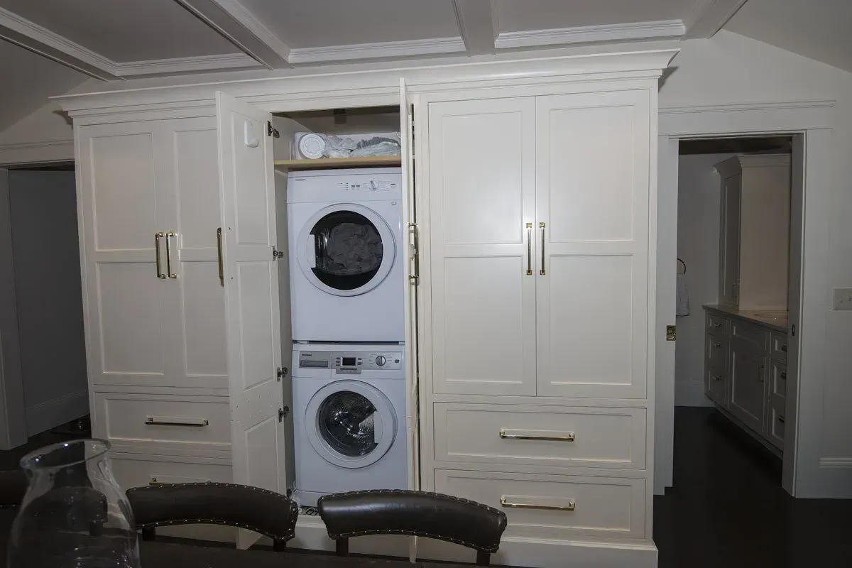 White laundry machines stacked in custom cabinetry, partially open.
