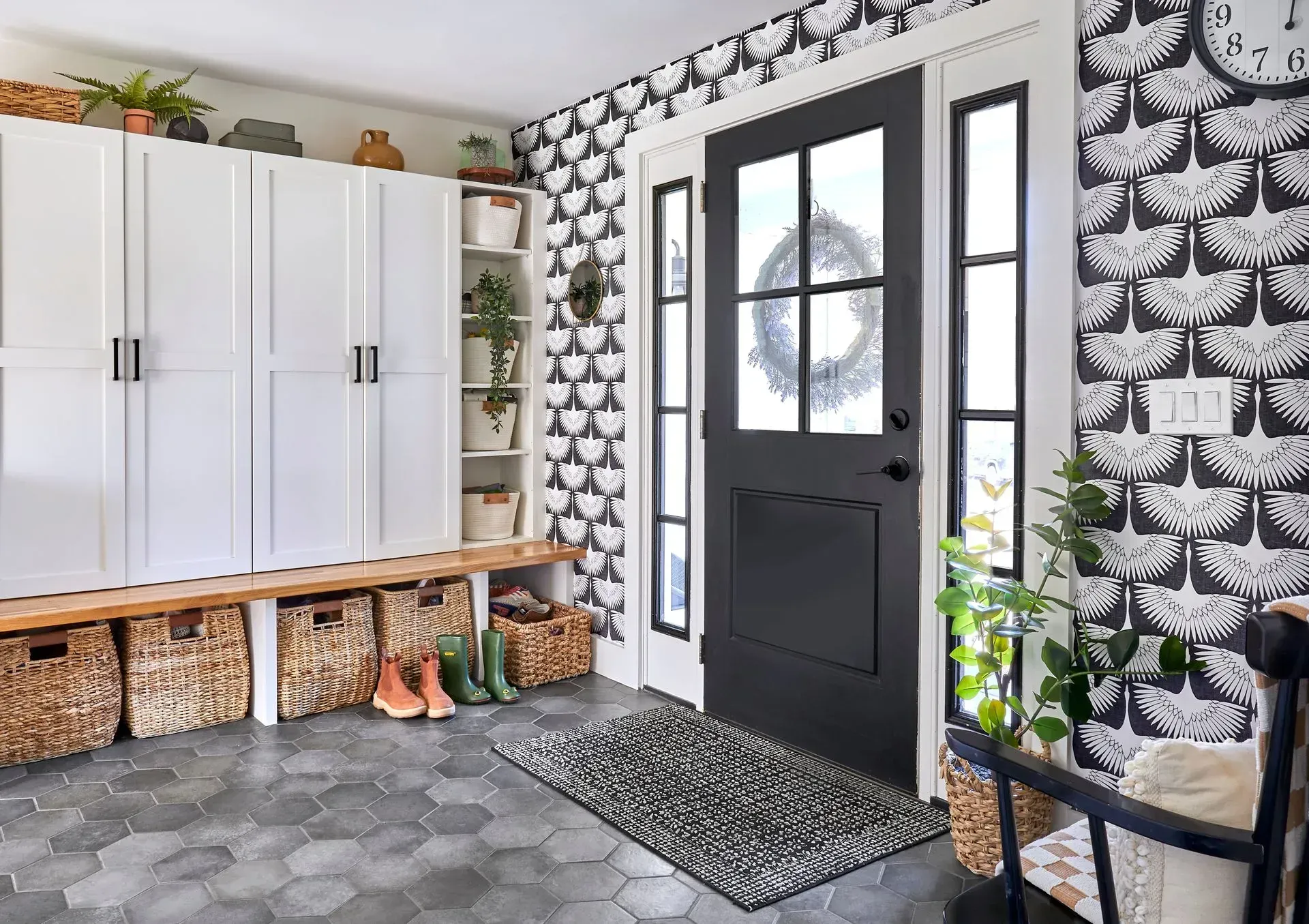 Entryway with black door, white cabinets, patterned wallpaper, and hexagon tile floor.