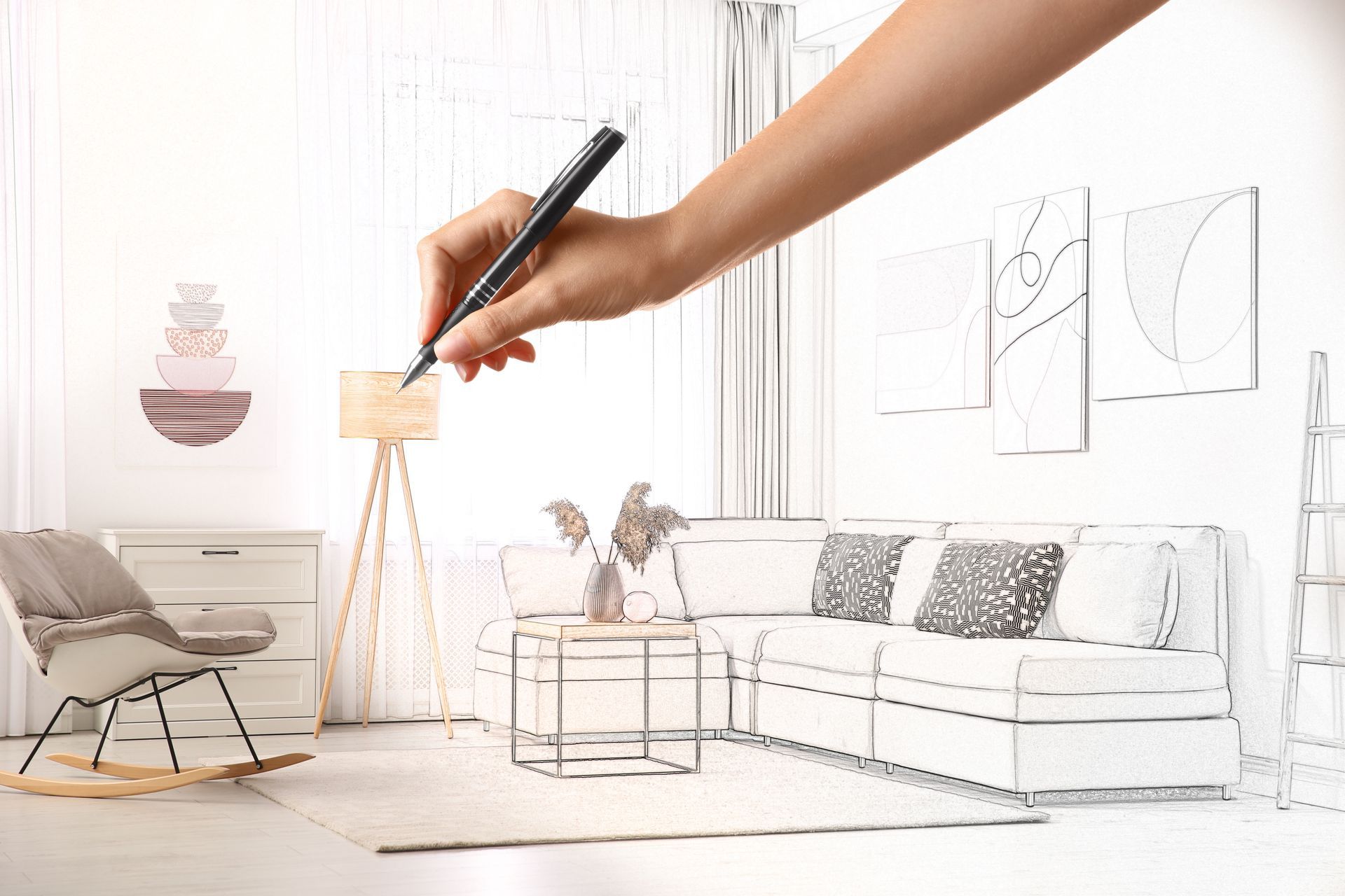 A hand sketching a living room interior with a pen, featuring furniture and decor.