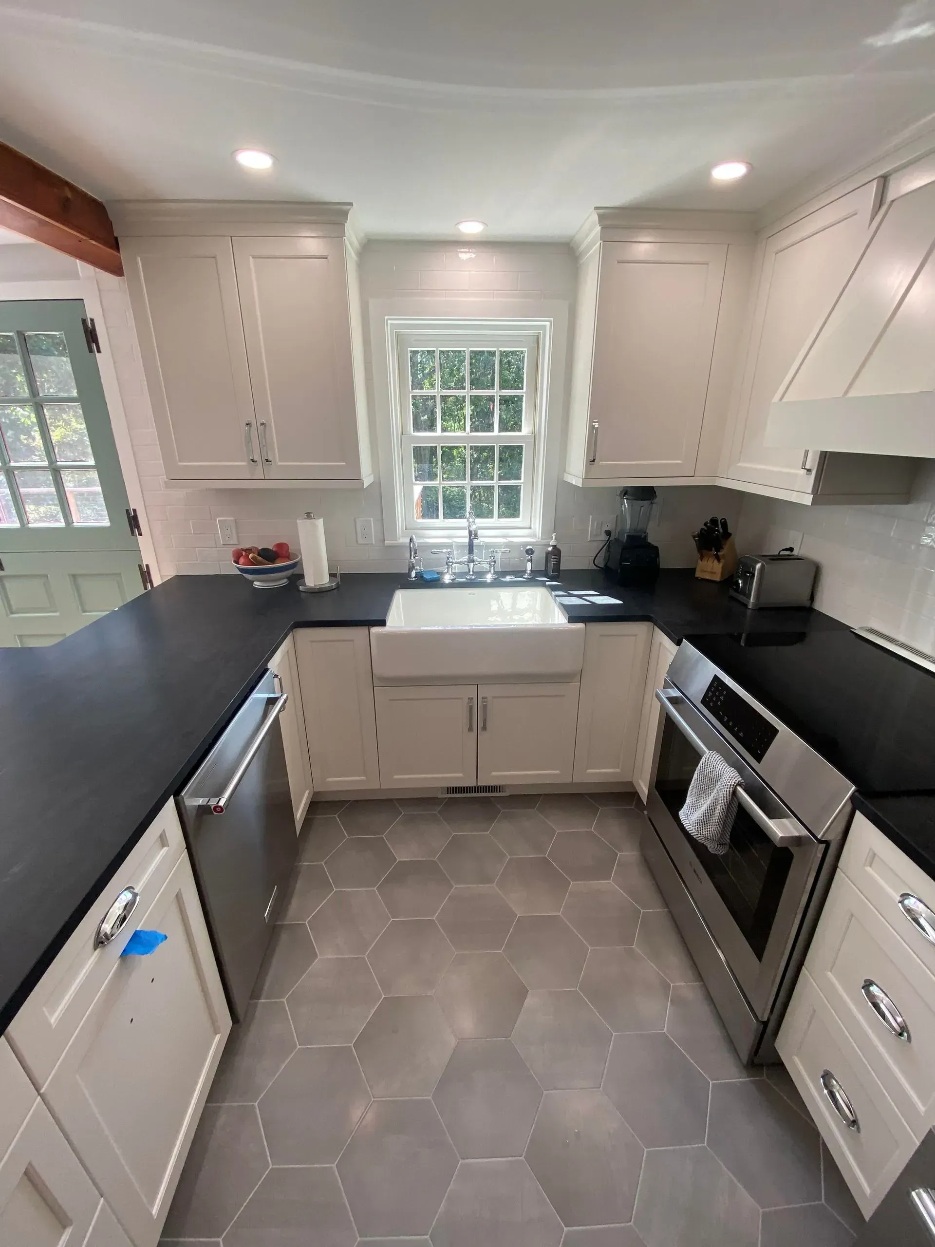U-shaped kitchen with white cabinets, dark countertops, stainless steel appliances, and gray hexagonal tile floor.