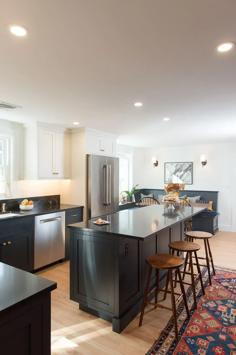 Modern kitchen with black island and countertops, stainless steel appliances, and wooden stools.