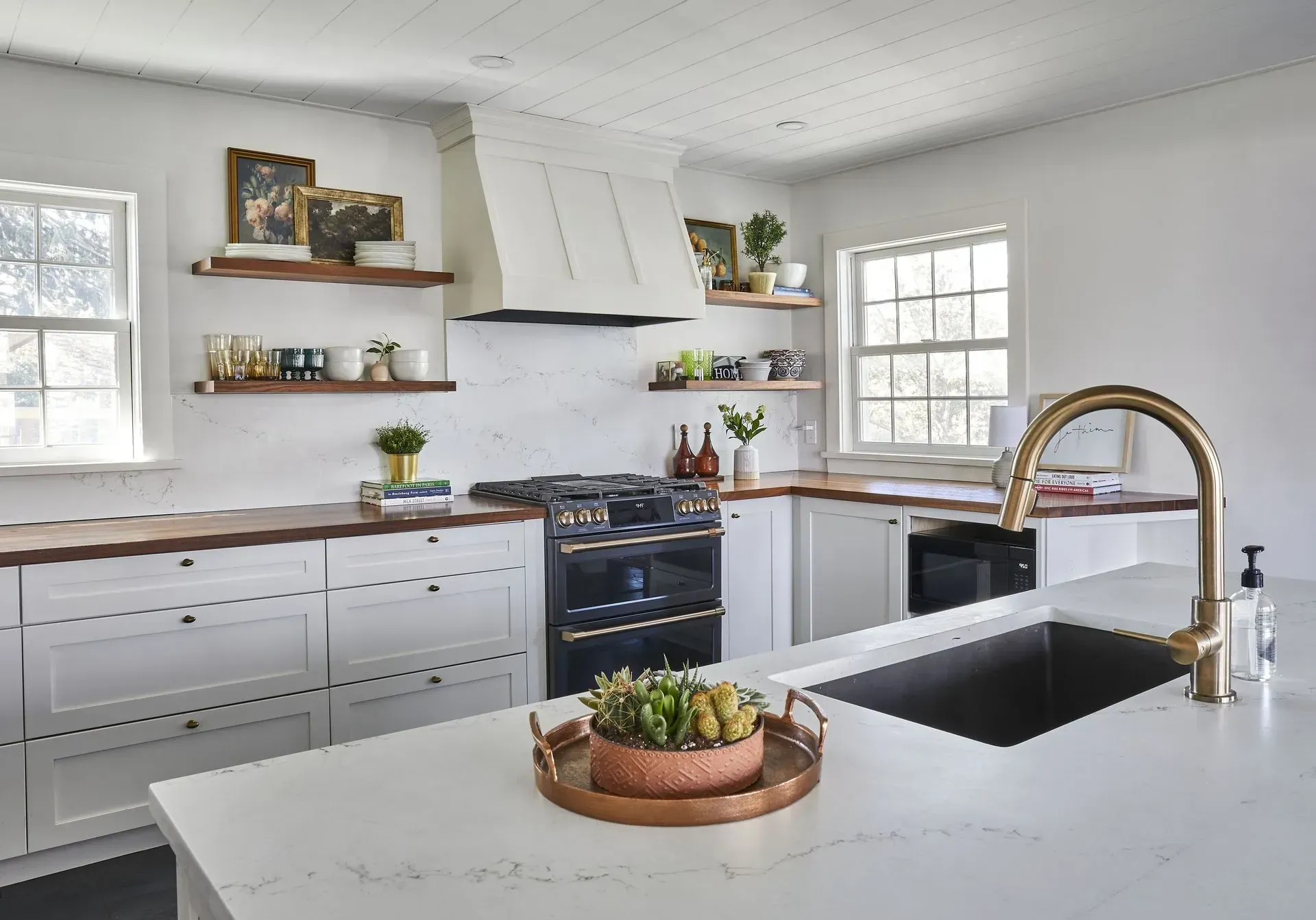 White kitchen with dark wood countertops, open shelves, and a large gold faucet.
