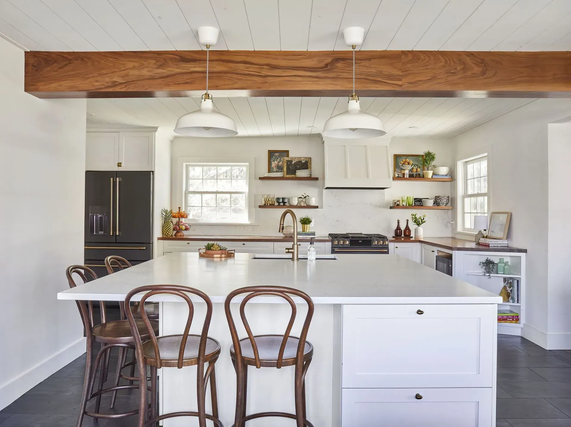 Bright farmhouse kitchen with white cabinetry, large island, wood beam, and bar stools.