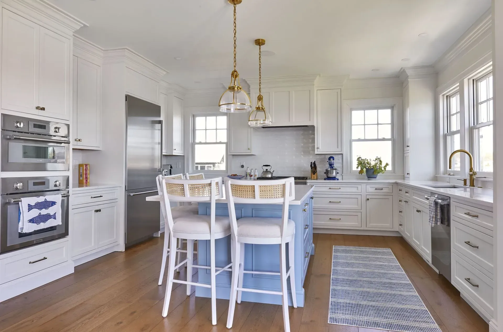 White kitchen with blue island, pendant lights, stainless steel appliances, and wooden floors.
