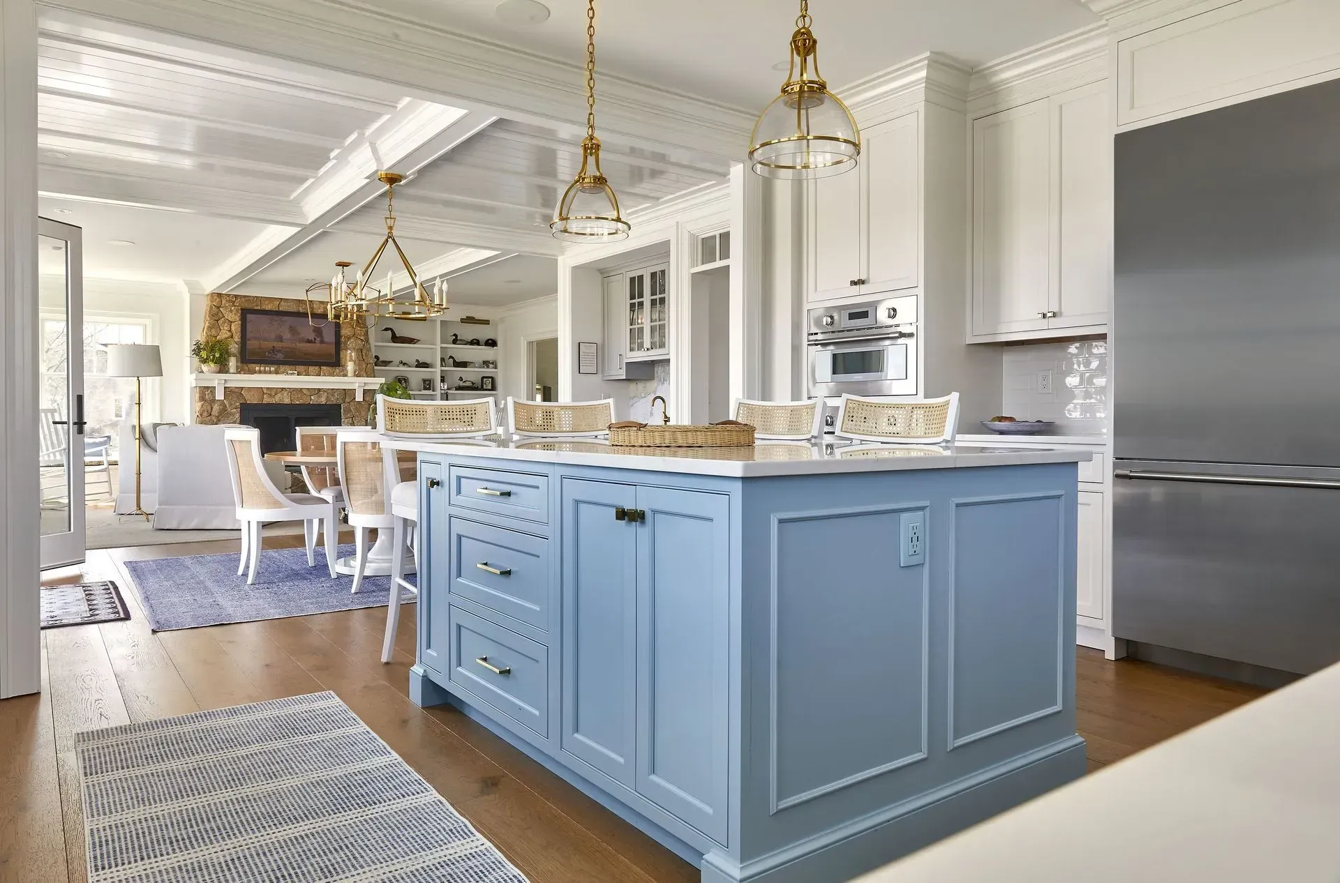 Blue and white kitchen with island, pendant lights, and stainless steel refrigerator.