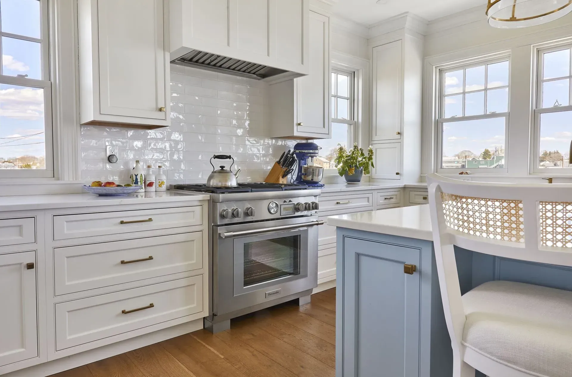 Bright white kitchen with stainless steel appliances, blue island, and light wood floors.