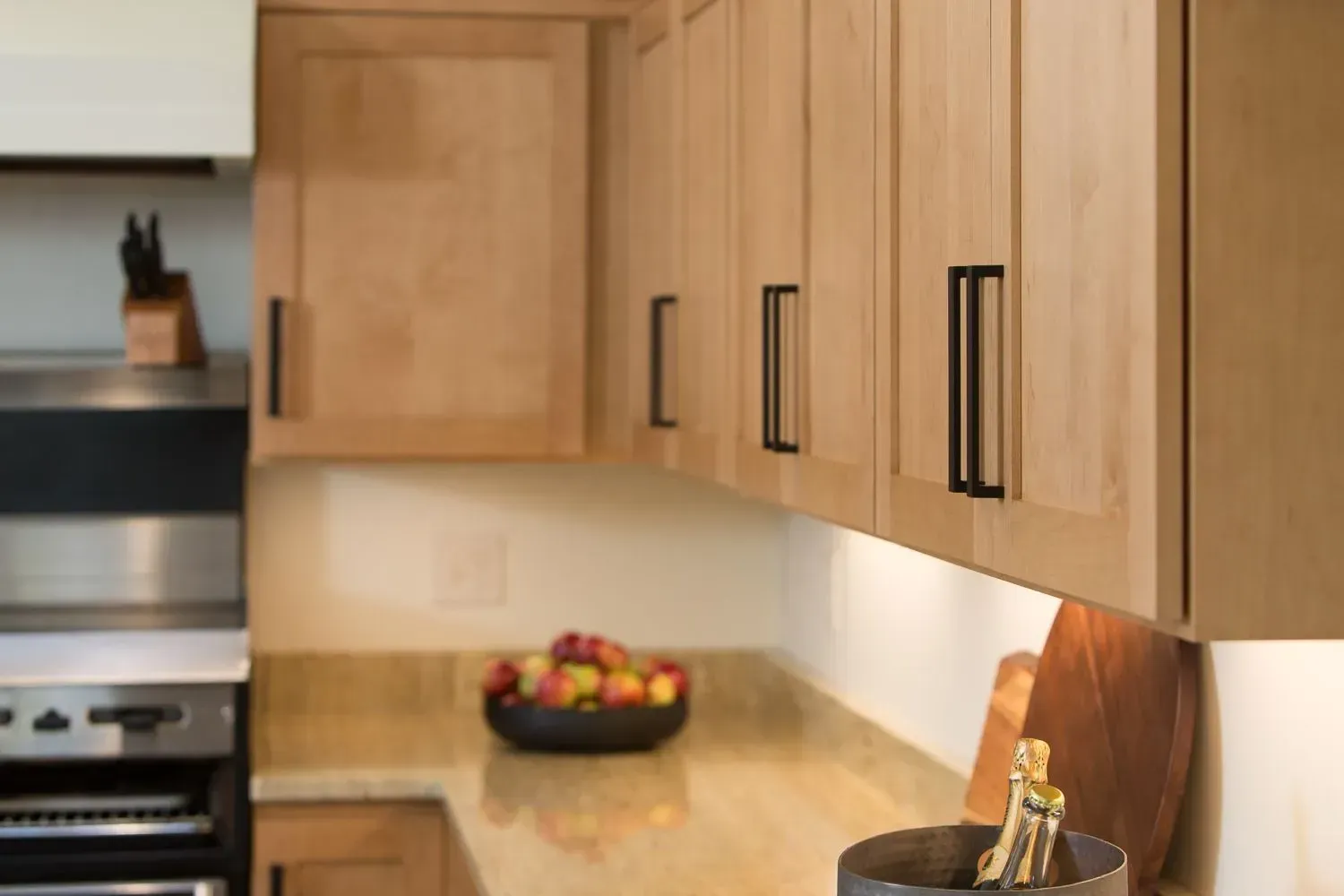 Kitchen cabinets with black handles, light wood, and a countertop with fruit.