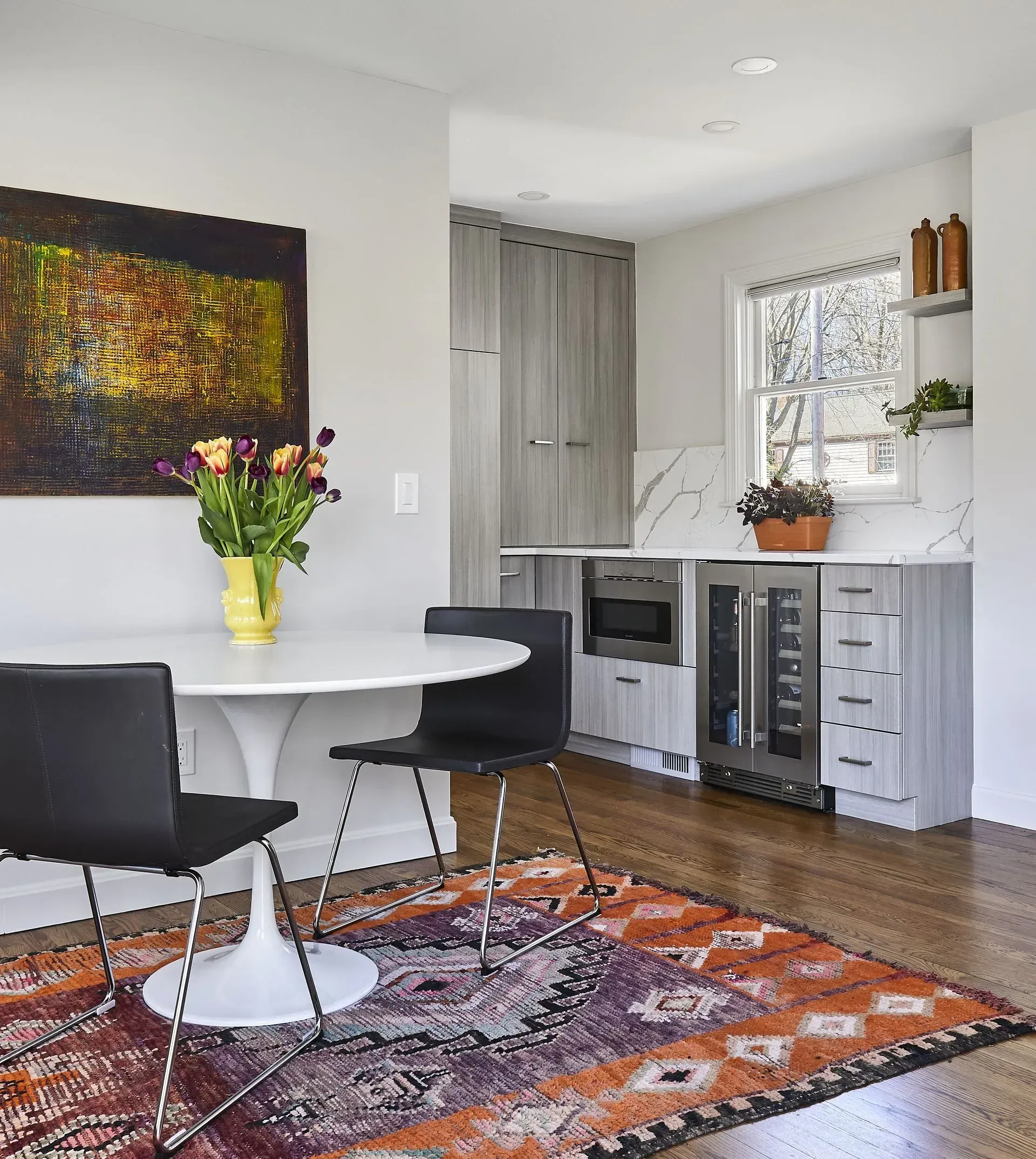 Dining area with white table, black chairs, colorful rug, artwork, and built-in bar with wine fridge.