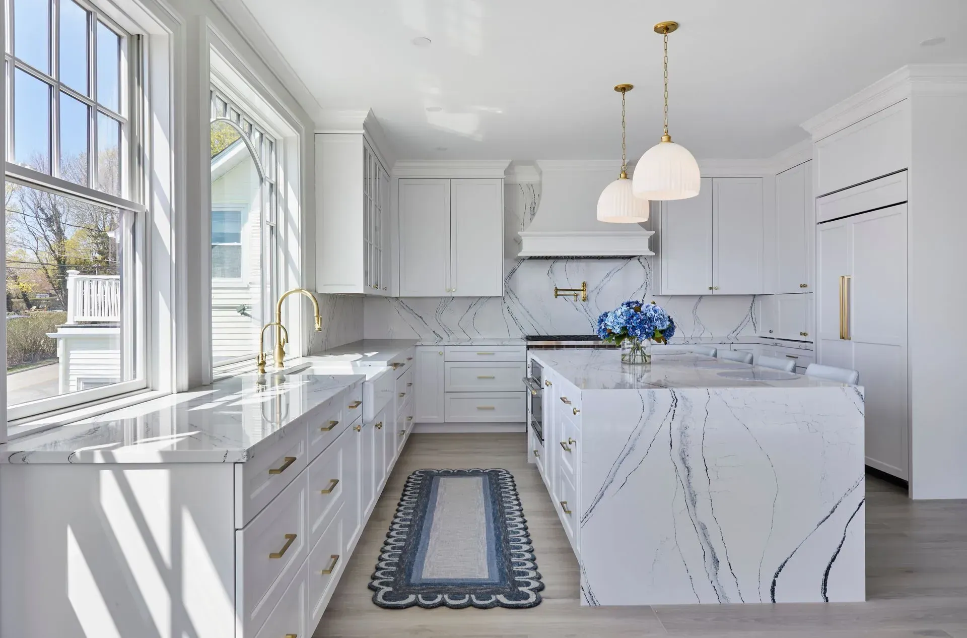 White kitchen with marble countertops, island, and cabinets. A window and gold accents are visible.