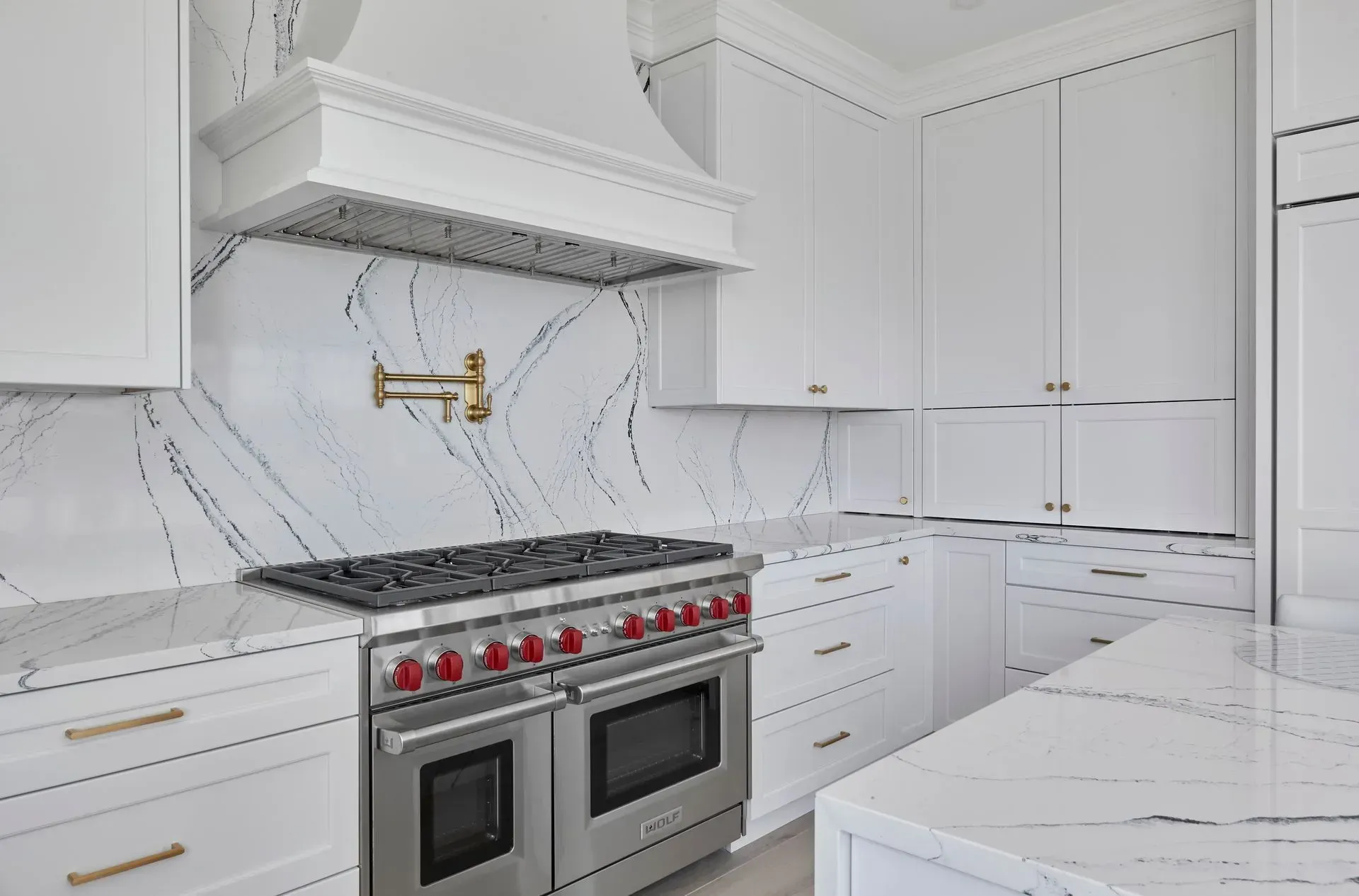 White kitchen with marble backsplash, stainless steel appliances, and gold hardware.