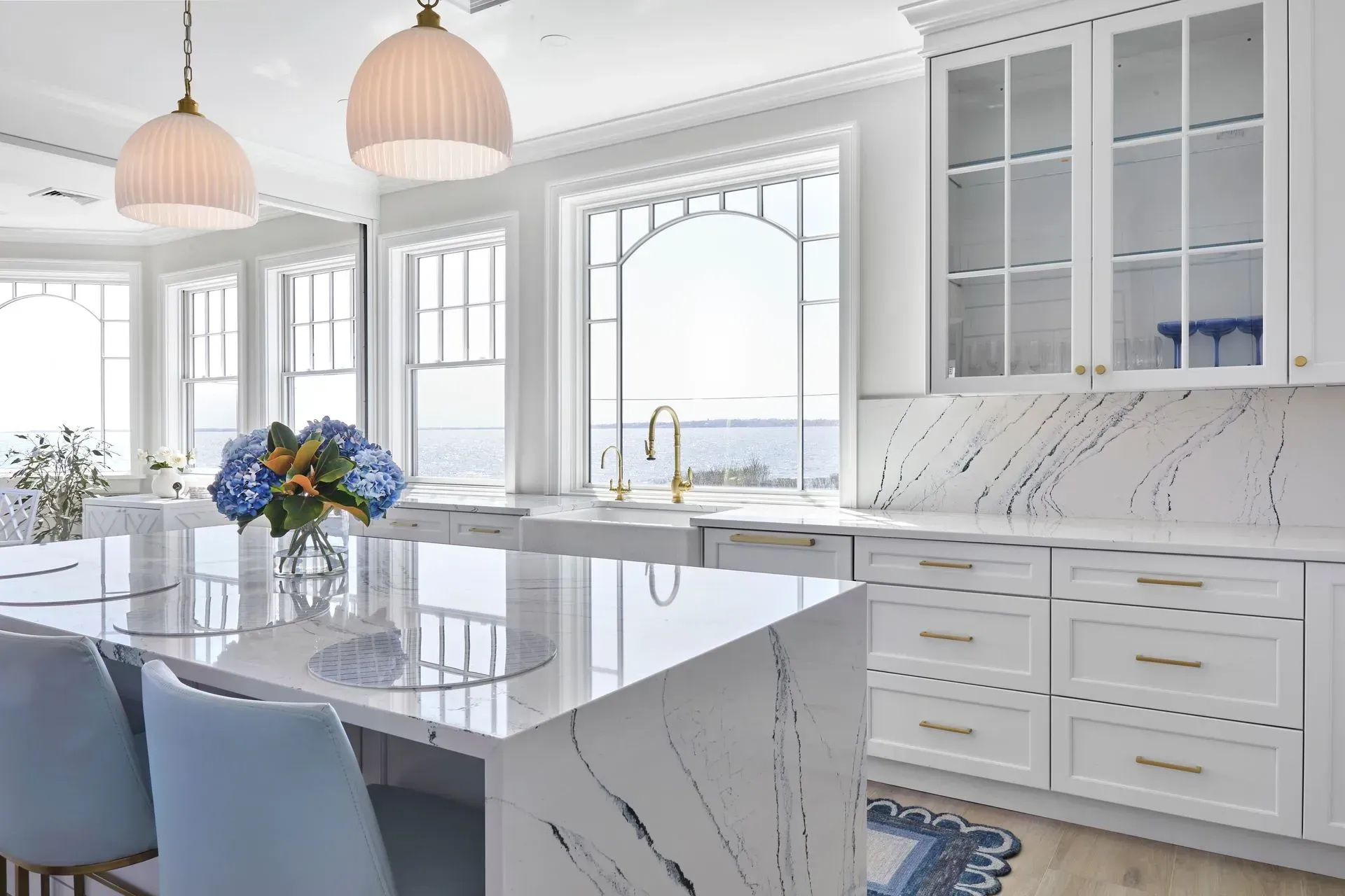Elegant white kitchen with marble countertops, blue accents, and a water view.