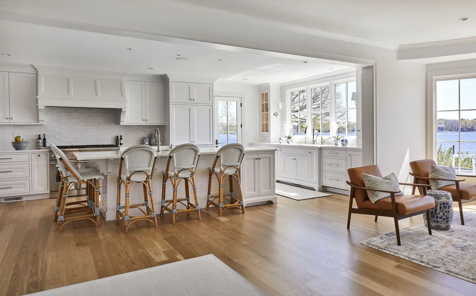 Bright, white kitchen and living room with island seating, hardwood floors, and water view.