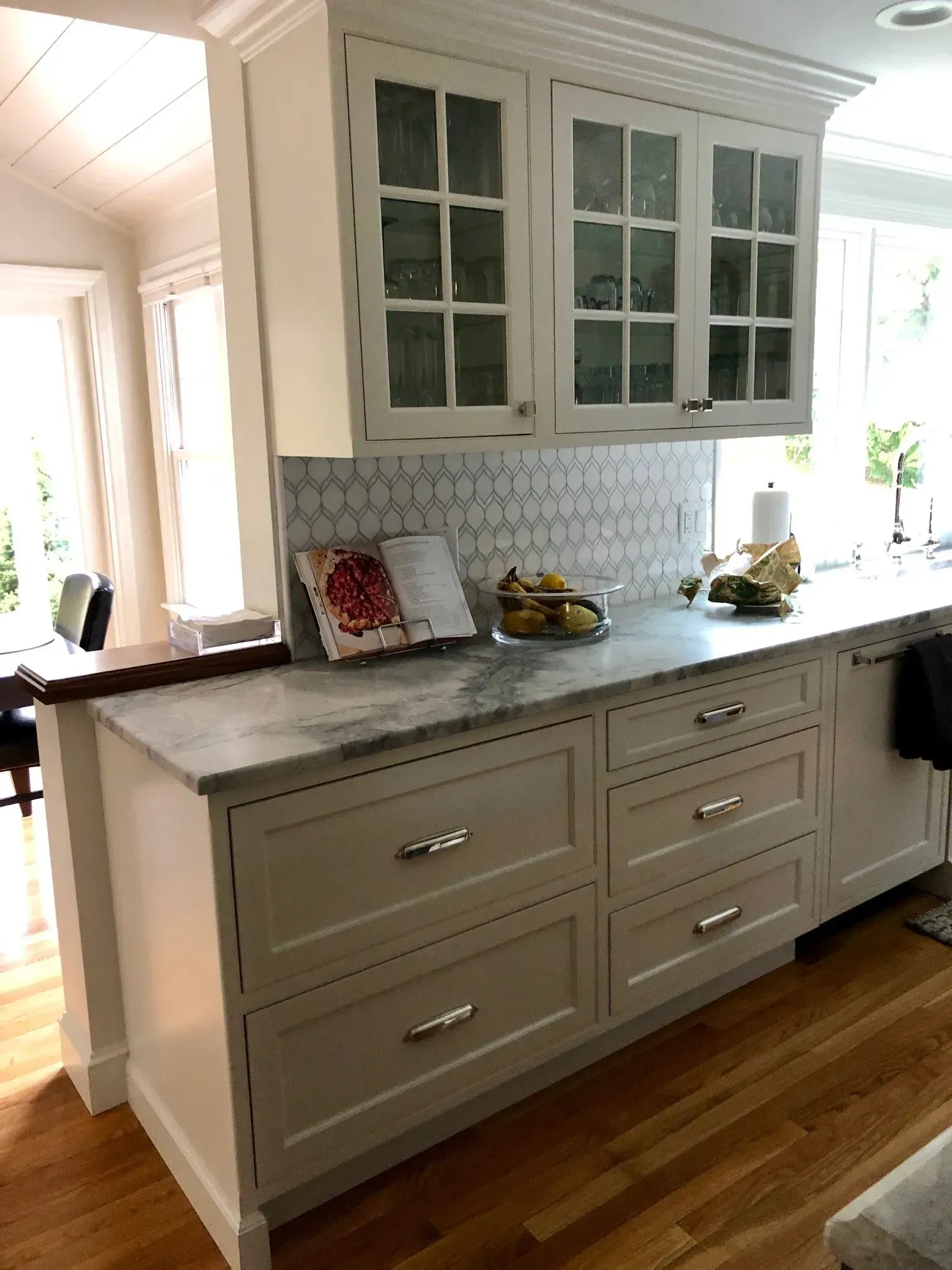 Kitchen with white cabinets, marble countertop, glass-front upper cabinets, and hexagon tile backsplash.