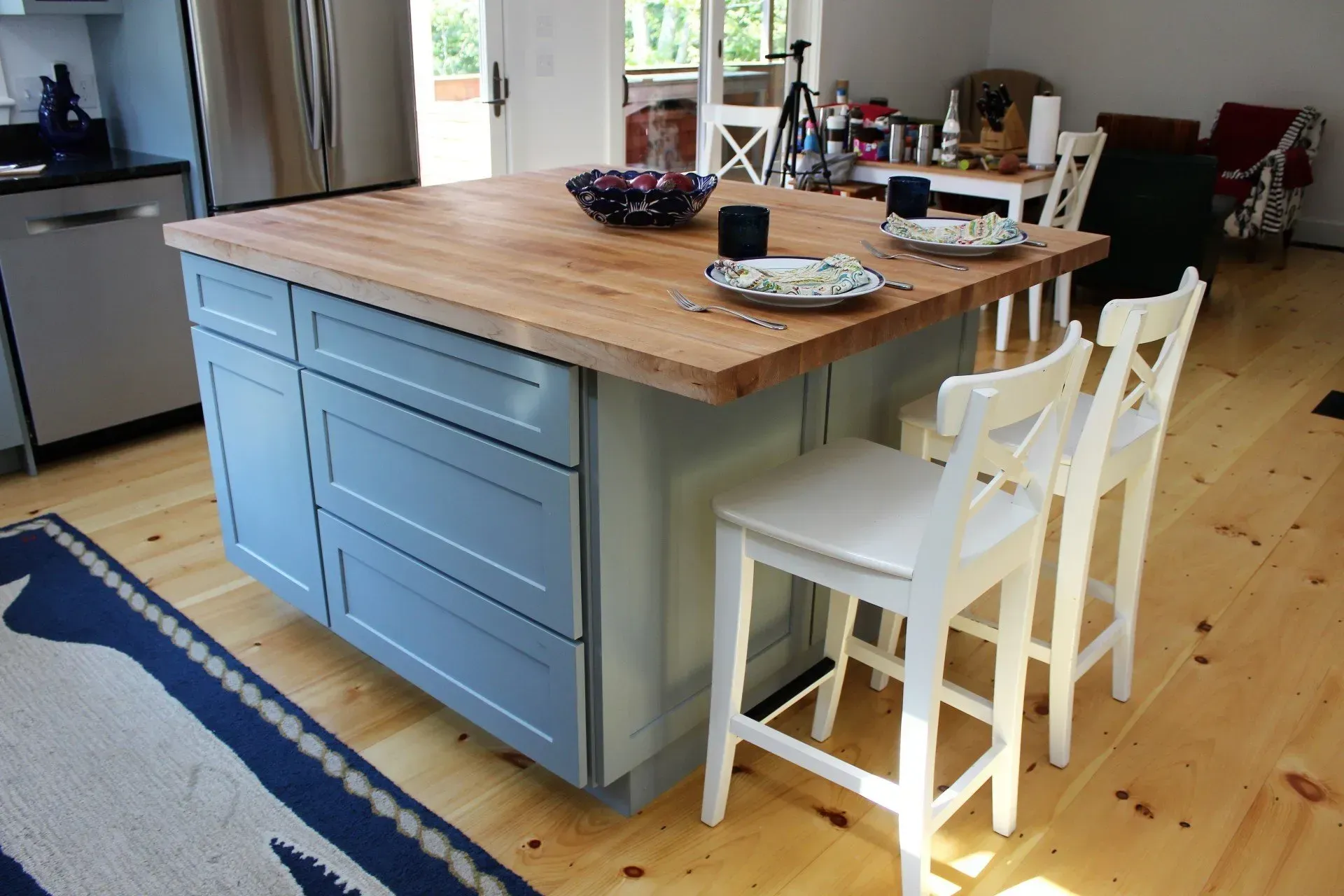 Kitchen island with blue cabinets, wood countertop, and white bar stools.