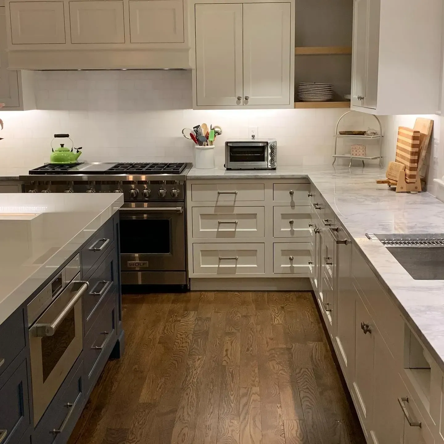 Kitchen with white and blue cabinets, stainless steel appliances, and dark wooden floors.