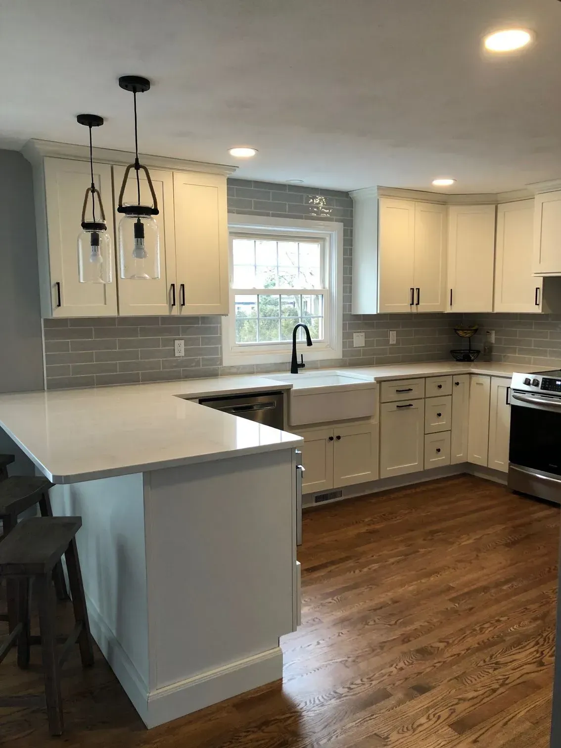 White kitchen with light wood floors, white cabinets, gray backsplash, and black pendant lights.