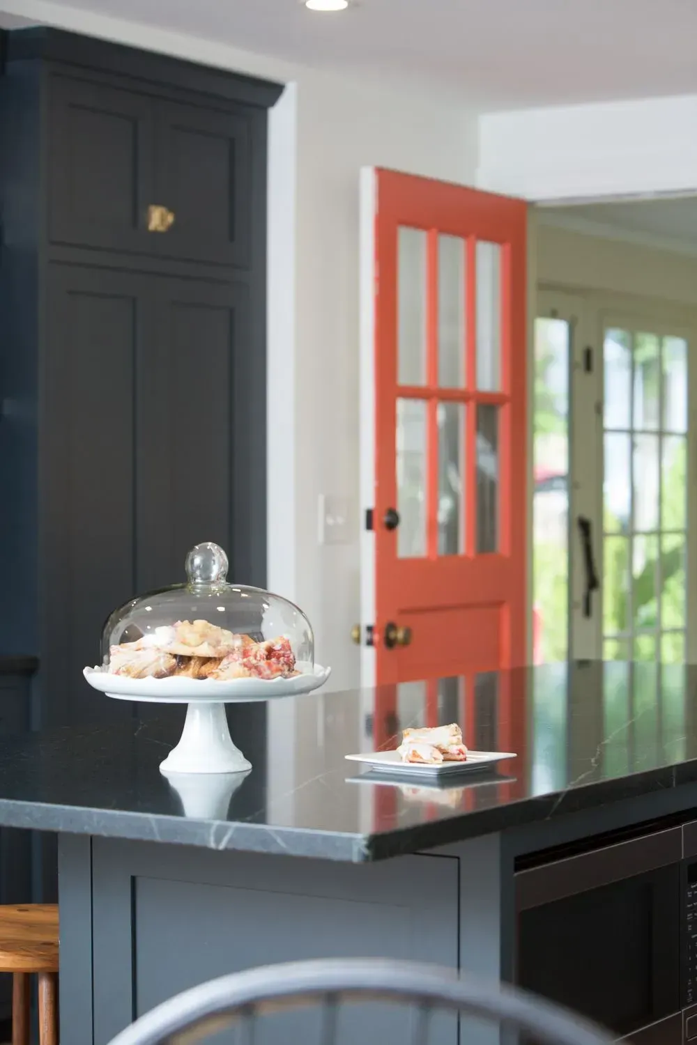 Kitchen island with baked goods, dark cabinets, and an orange door.