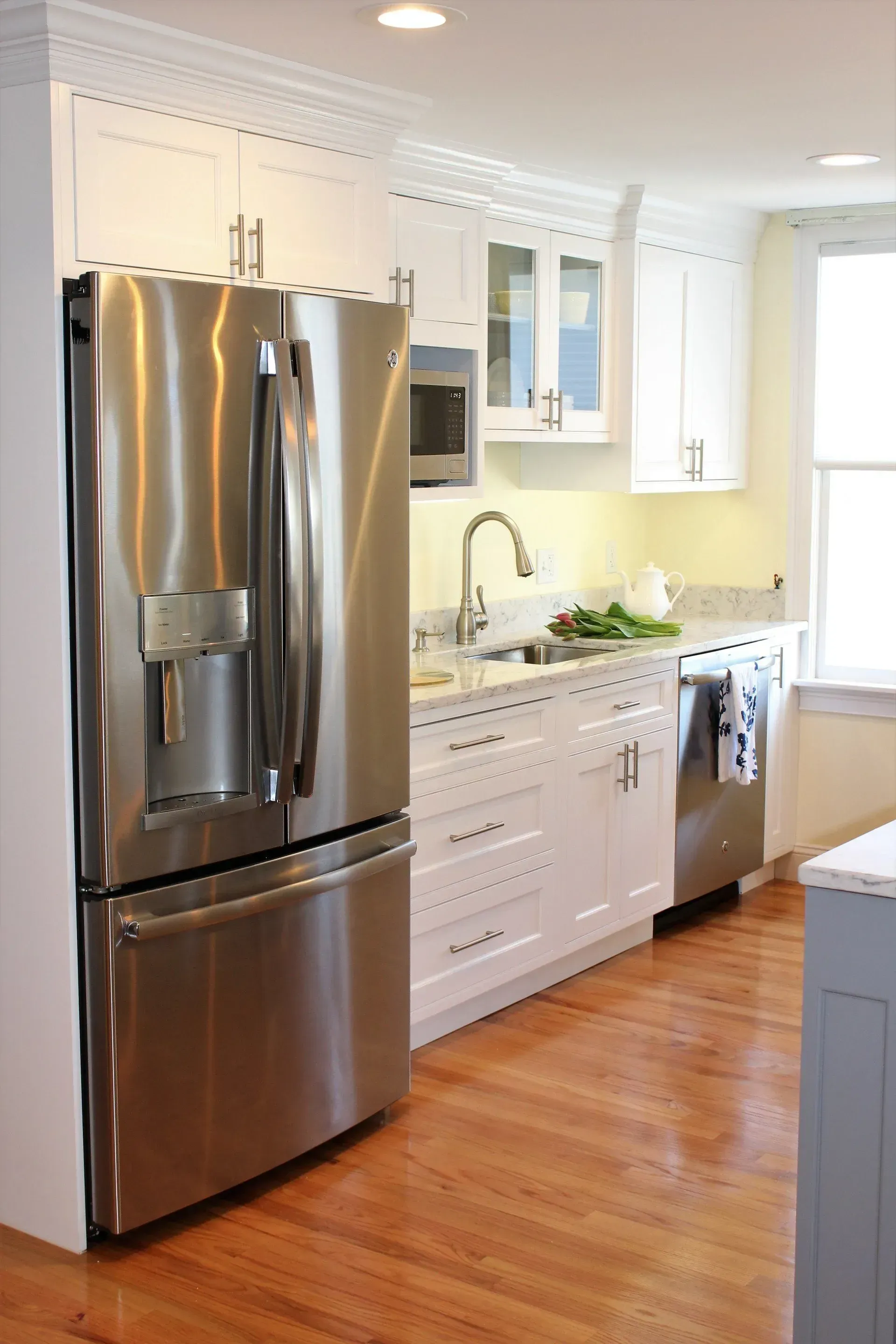 Stainless steel refrigerator in a white kitchen with wood floors and granite countertops.