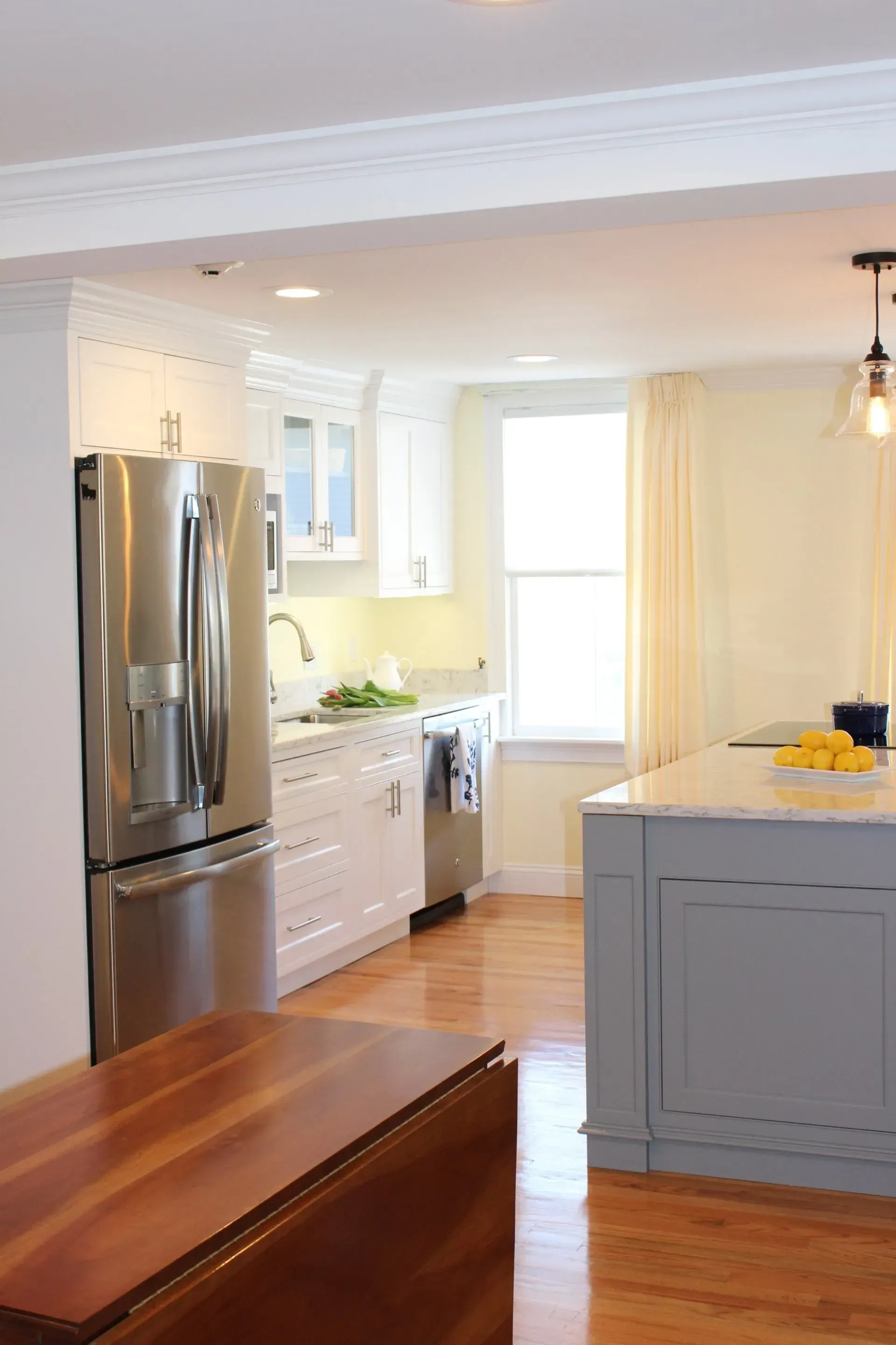 Modern white kitchen with stainless steel appliances, grey island, and hardwood floors.