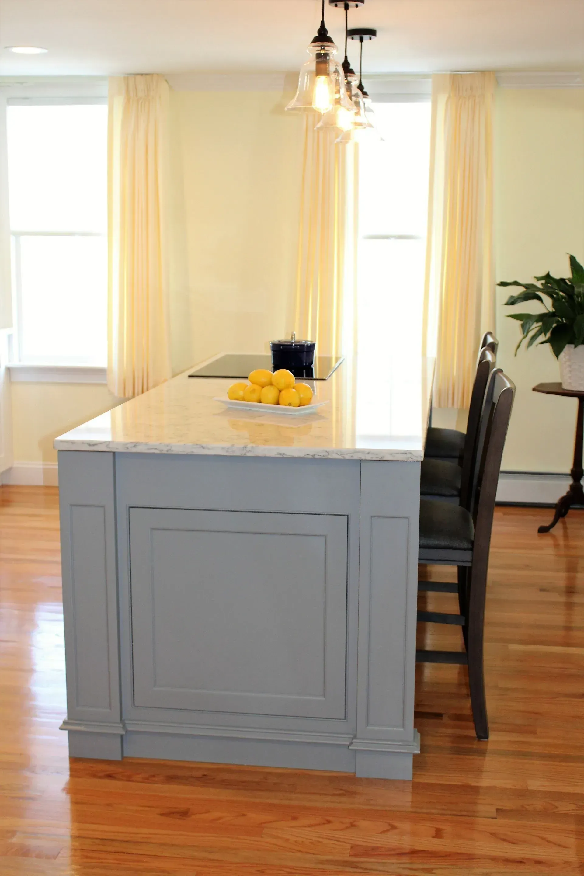 Gray kitchen island with a light countertop, two stools, and hanging lights. Yellow walls, wood floors.