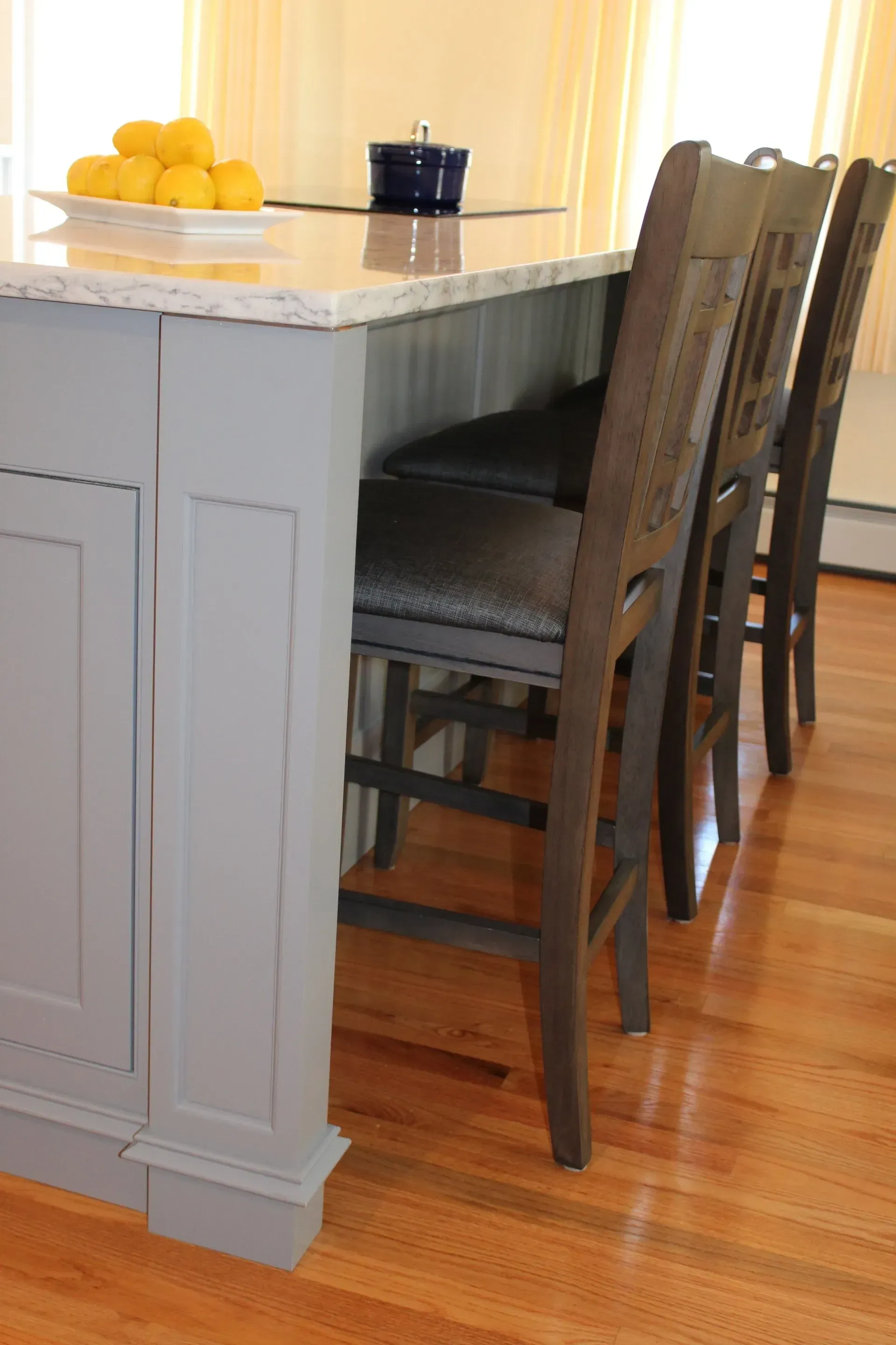 Gray kitchen island with three dark wooden bar stools on a hardwood floor.